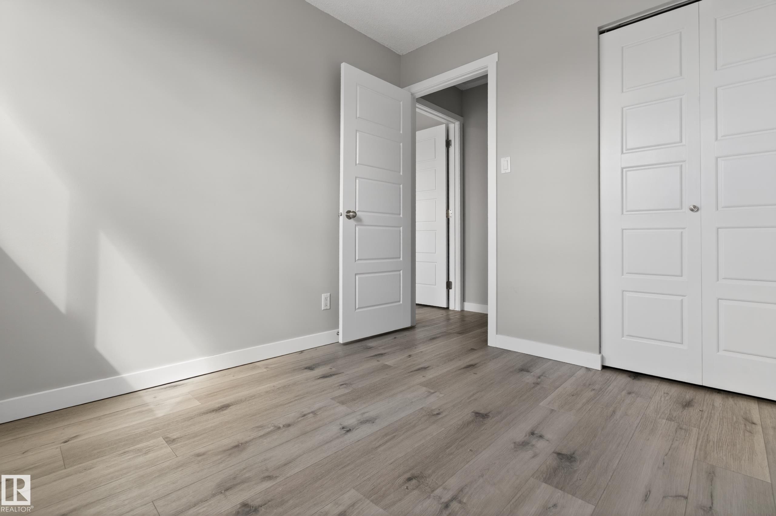 Room featuring wood-finish flooring, light grey painted walls, white trim, and a white paneled door - 18 Lakewood Village, Edmonton, AB - Indoor Photo Showing Other Room