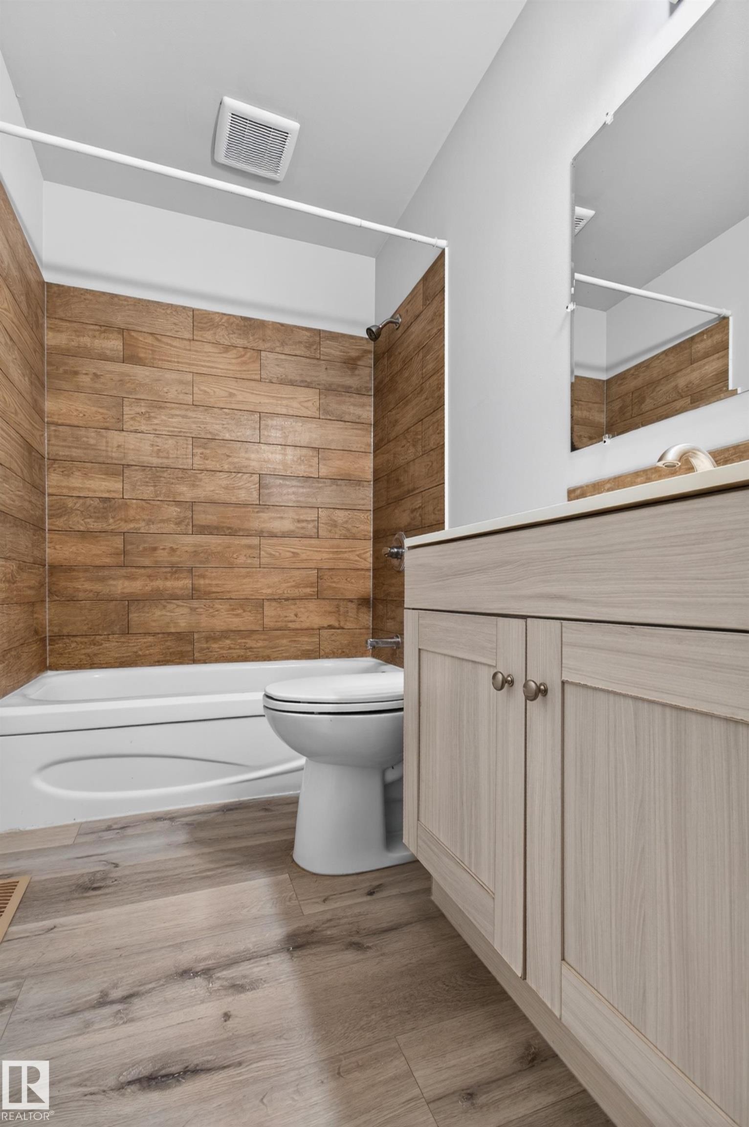 Bathroom featuring a white bathtub, wood-finish wall tile, light wood-finish vanity with cabinet storage, light-toned countertop, and wood-finish flooring - 18 Lakewood Village, Edmonton, AB - Indoor Photo Showing Bathroom
