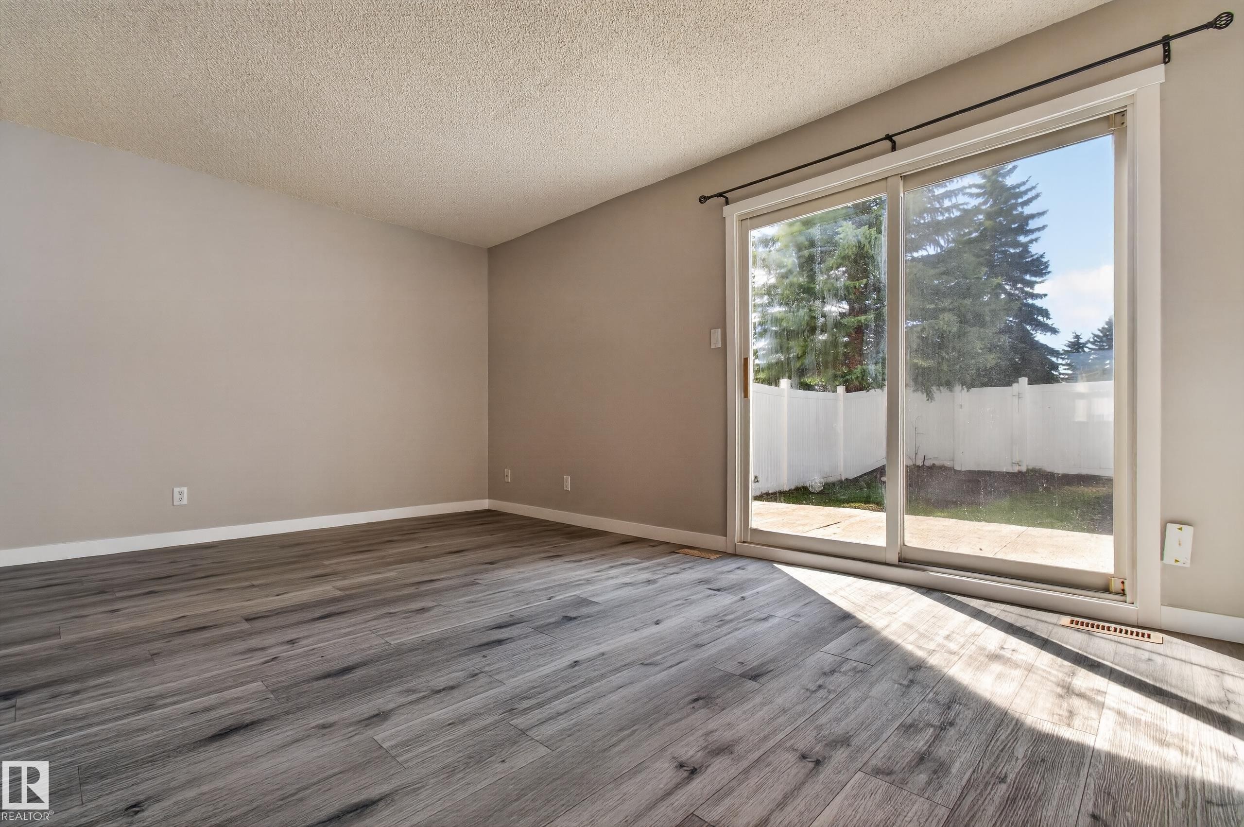 Spacious interior featuring wood-finish flooring, neutral wall tones, and a large sliding glass door - 18 Lakewood Village, Edmonton, AB - Indoor Photo Showing Other Room