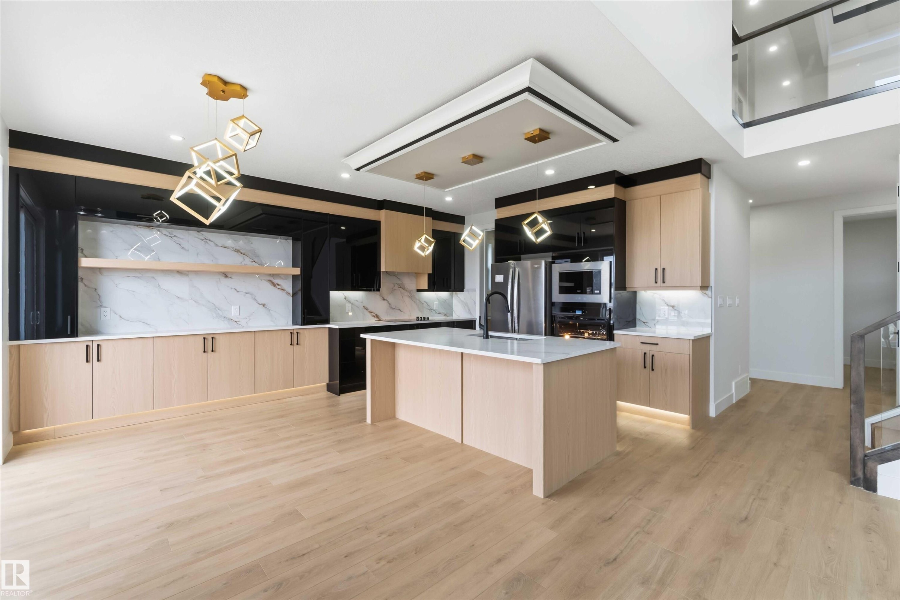 Modern kitchen featuring a central island with a light-toned countertop, wood-finish cabinetry, integrated stainless steel appliances, a marble-look backsplash, and unique geometric pendant lighting - 417 Pine Point(E), Leduc, AB - Indoor Photo Showing Kitchen With Upgraded Kitchen