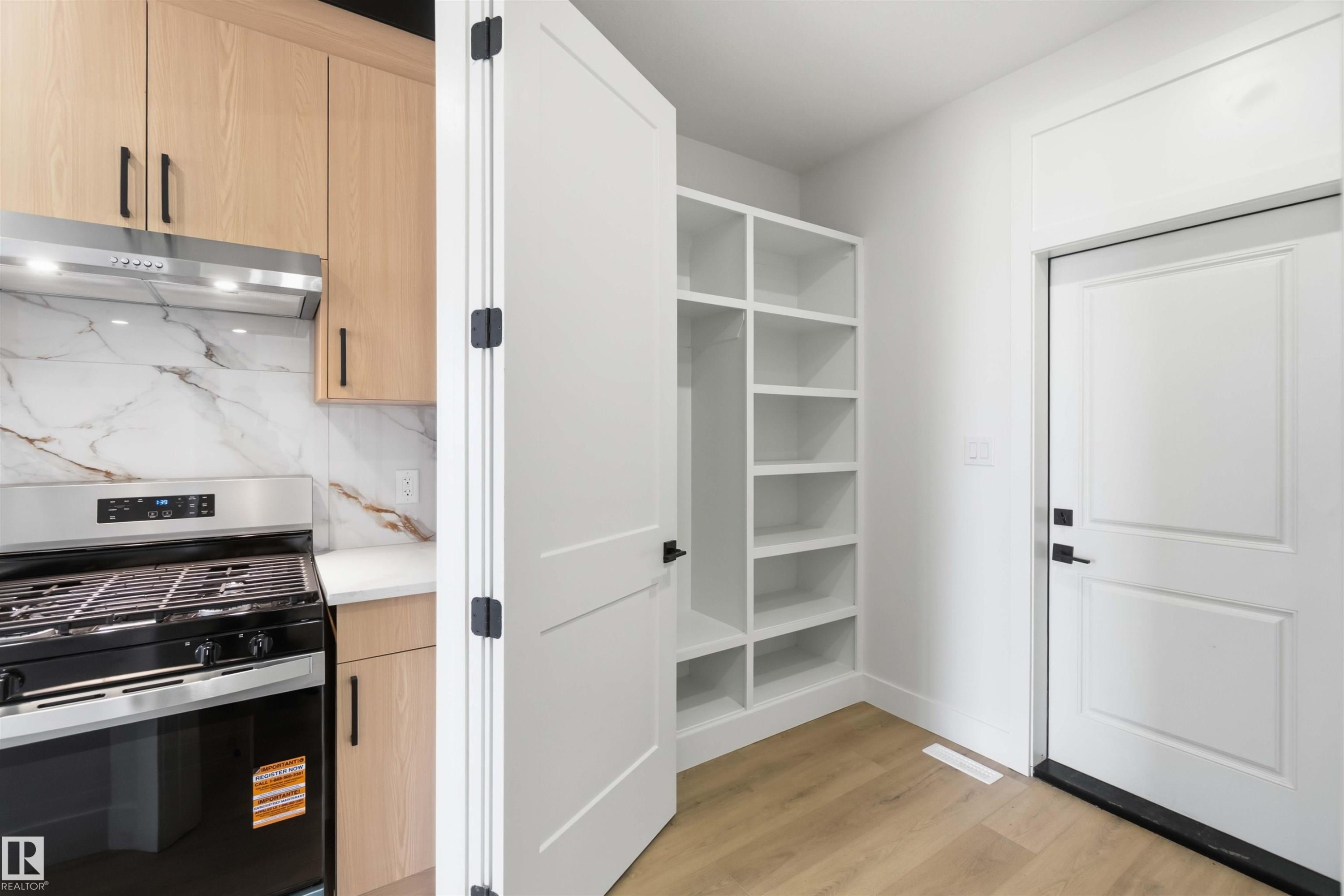 Kitchen area featuring a stainless steel range with overhead ventilation, light wood-finish cabinetry, and a white countertop - 417 Pine Point(E), Leduc, AB - Indoor