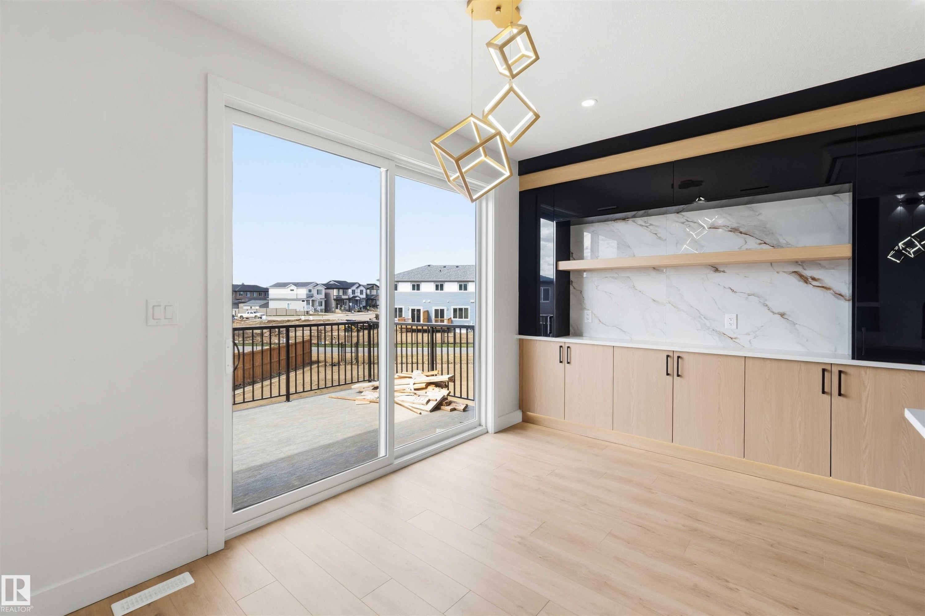 Spacious room featuring light wood-finish flooring, a wall of built-in cabinetry with a white countertop and marble-patterned backsplash, and a modern geometric light fixture - 417 Pine Point(E), Leduc, AB - Indoor Photo Showing Other Room