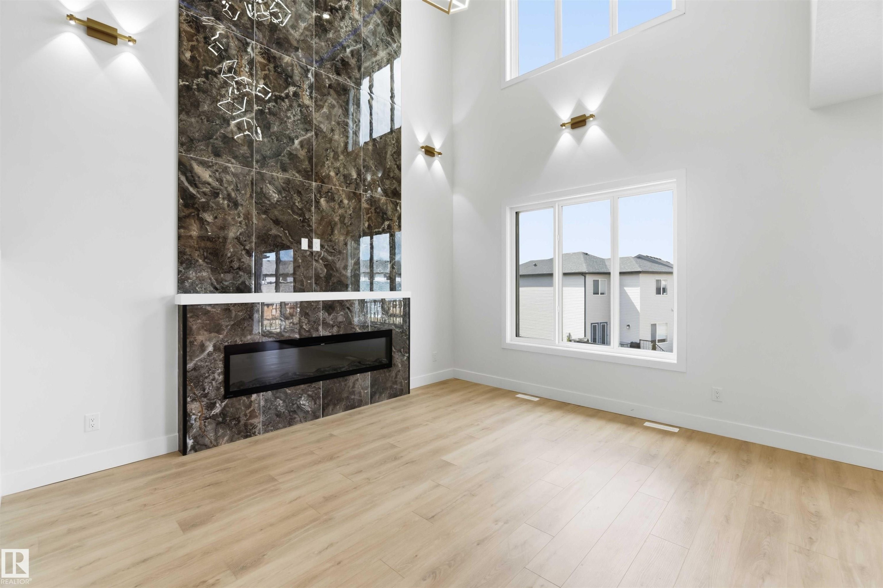 High-ceiling interior space featuring a full-height dark marble-patterned fireplace surround with a linear electric insert - 417 Pine Point(E), Leduc, AB - Indoor With Fireplace