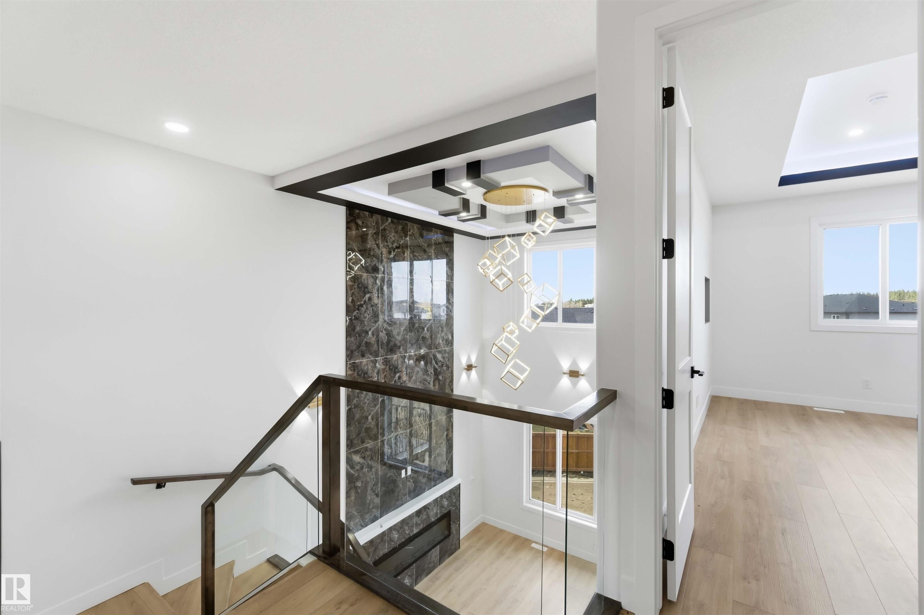 Stairwell featuring glass railings, wood-finish treads, and a modern chandelier - 417 Pine Point(E), Leduc, AB - Indoor Photo Showing Other Room