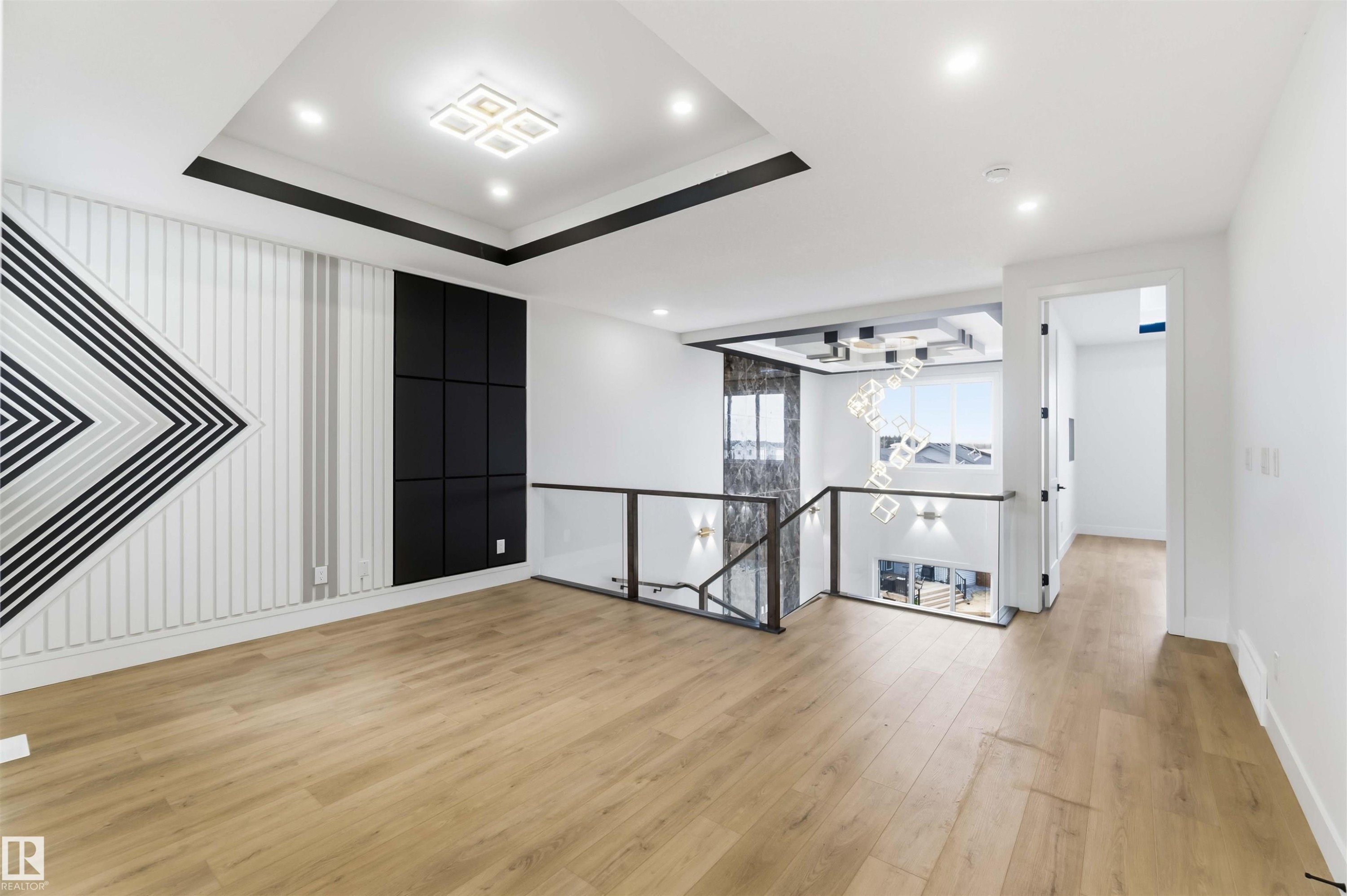 Open-concept living space featuring wood-finish flooring, a tiered ceiling with recessed lighting and a central fixture, and a decorative wall with geometric paneling - 417 Pine Point(E), Leduc, AB - Indoor Photo Showing Other Room
