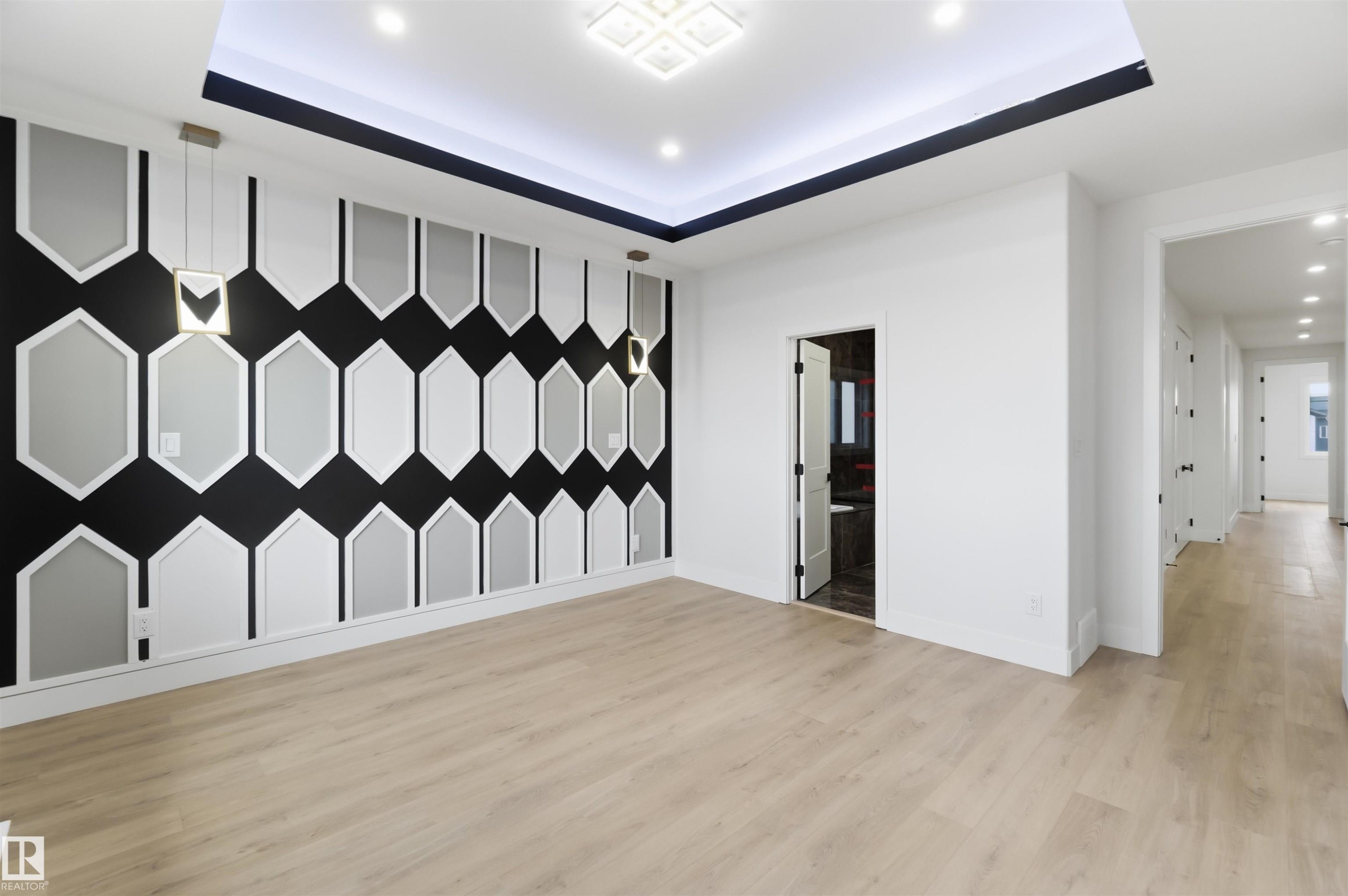 Open concept room featuring a decorative accent wall with geometric paneling, wood-finish flooring, a recessed tray ceiling with integrated lighting, and modern pendant light fixtures - 417 Pine Point(E), Leduc, AB - Indoor Photo Showing Other Room