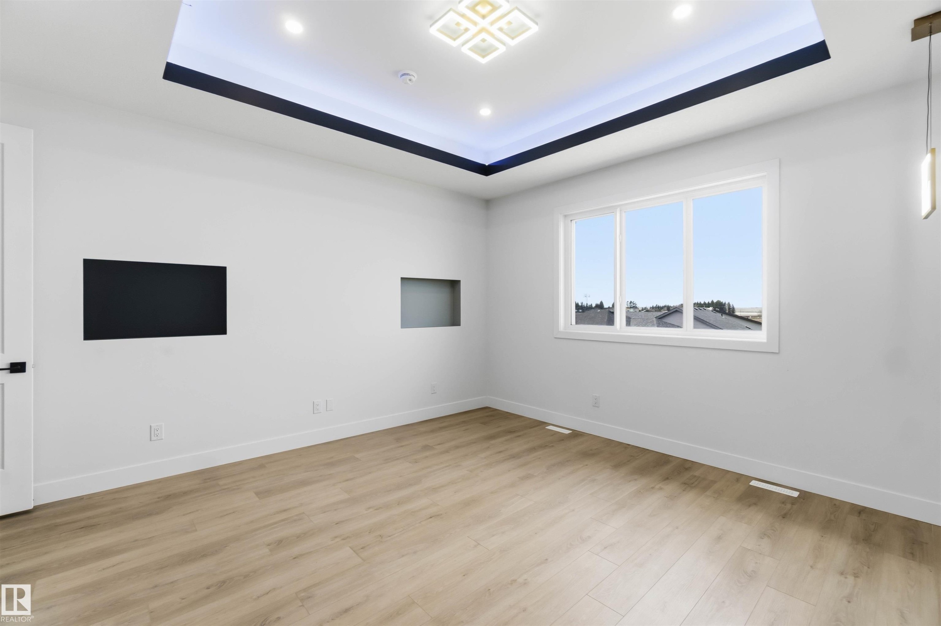 Spacious room featuring light wood-finish flooring, a tray ceiling with integrated lighting, and a large multi-pane window - 417 Pine Point(E), Leduc, AB - Indoor Photo Showing Other Room