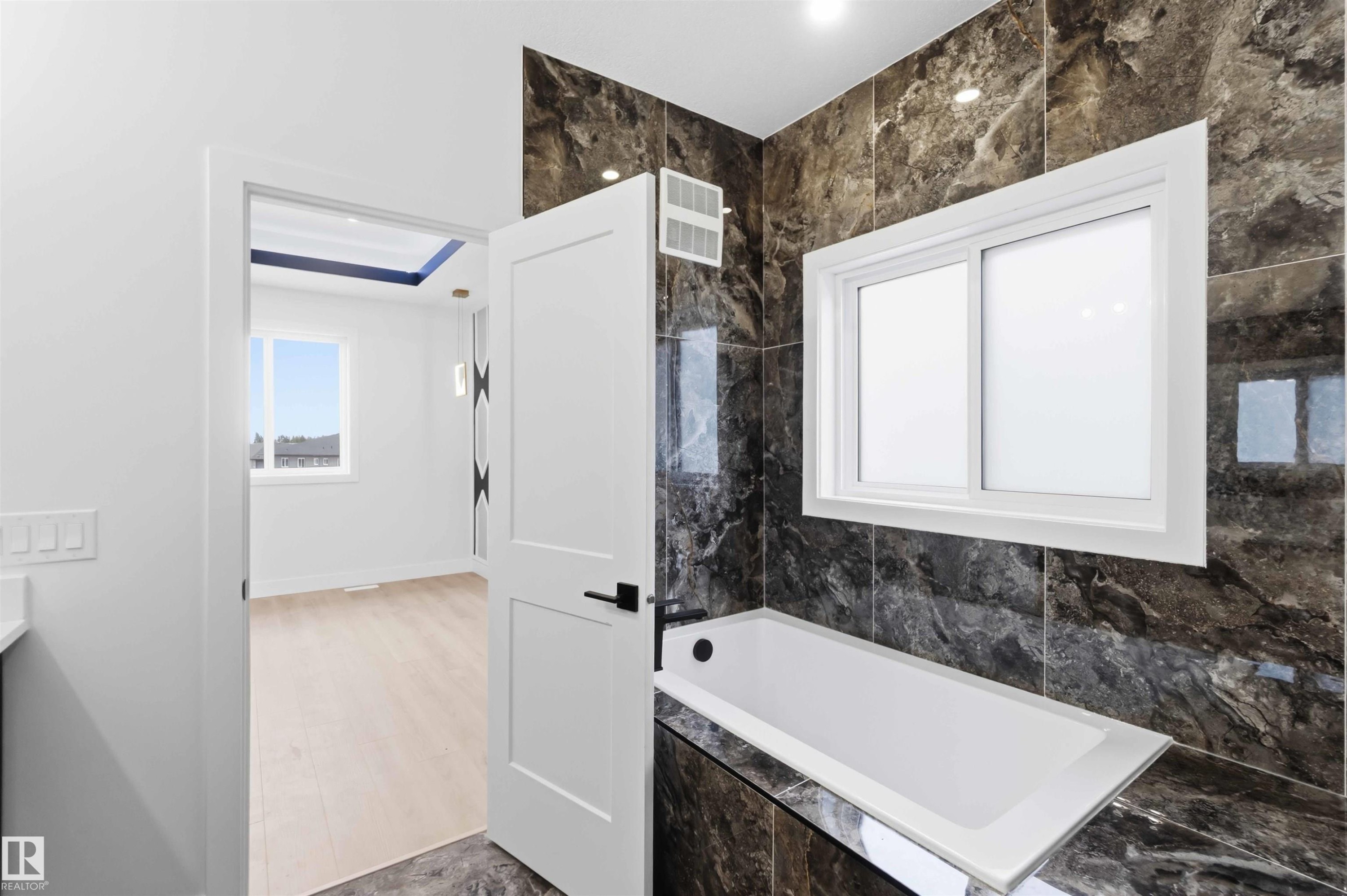 Bathroom featuring a built-in tub with dark marble-look tile surround and a sliding window - 417 Pine Point(E), Leduc, AB - Indoor Photo Showing Bathroom