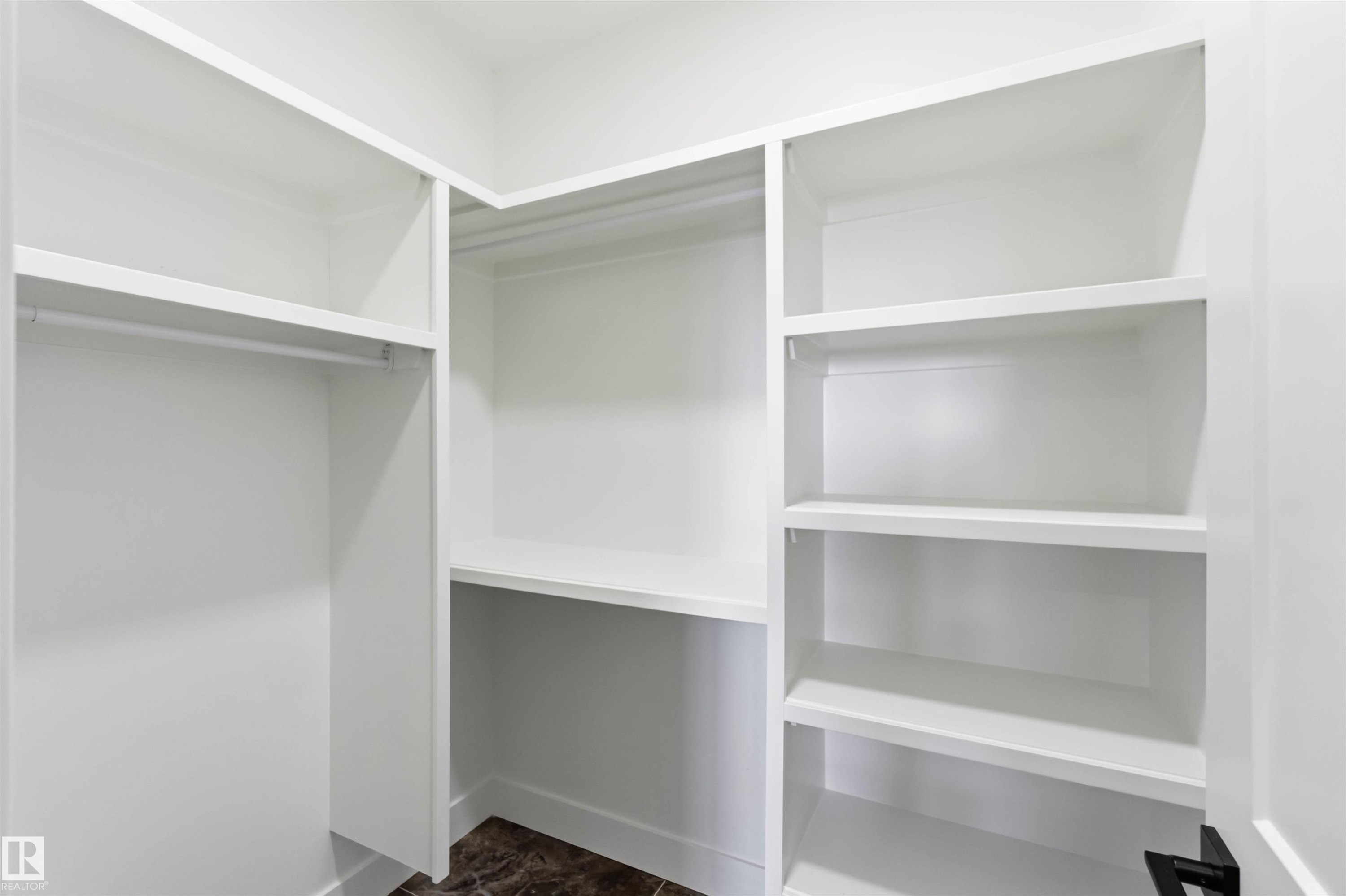Walk-in closet featuring white built-in shelving, hanging rods, and dark patterned flooring - 417 Pine Point(E), Leduc, AB - Indoor With Storage