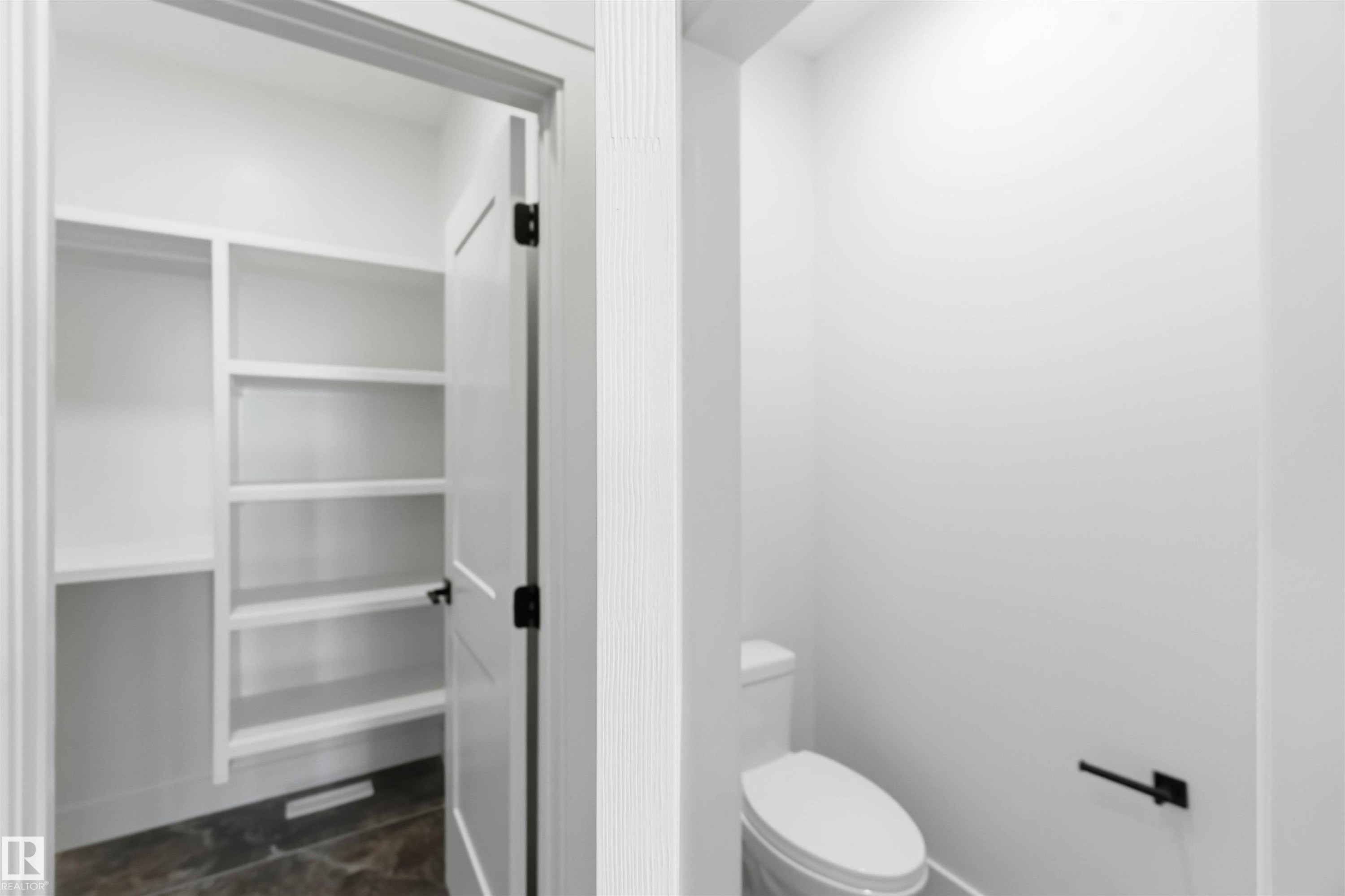 White built-in shelving with multiple levels, featuring a dark floor, and a white interior door with black hardware - 417 Pine Point(E), Leduc, AB - Indoor Photo Showing Bathroom