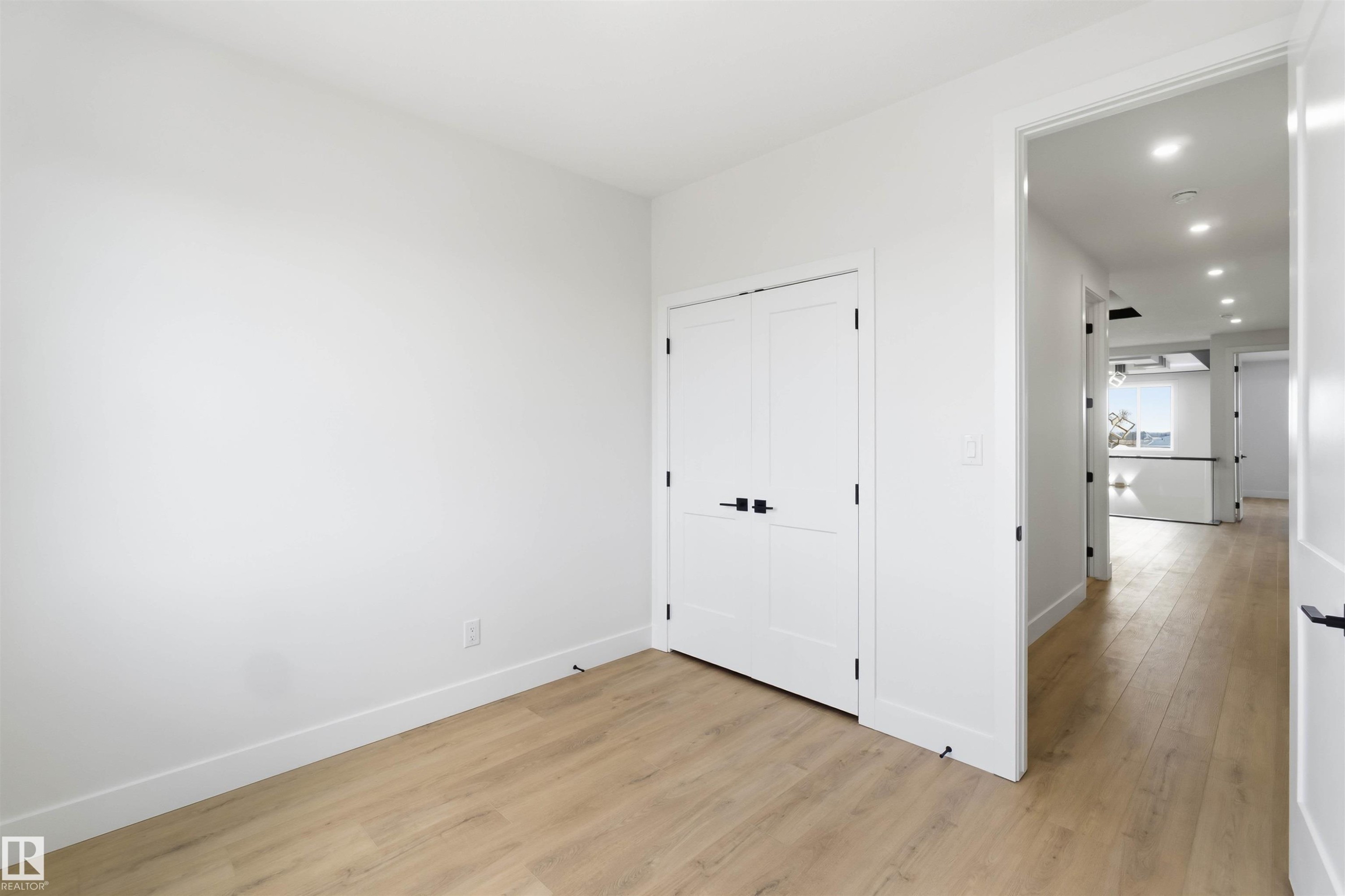 Room featuring light wood-finish flooring, white walls, and a pair of white bifold doors with matte black hardware - 417 Pine Point(E), Leduc, AB - Indoor Photo Showing Other Room