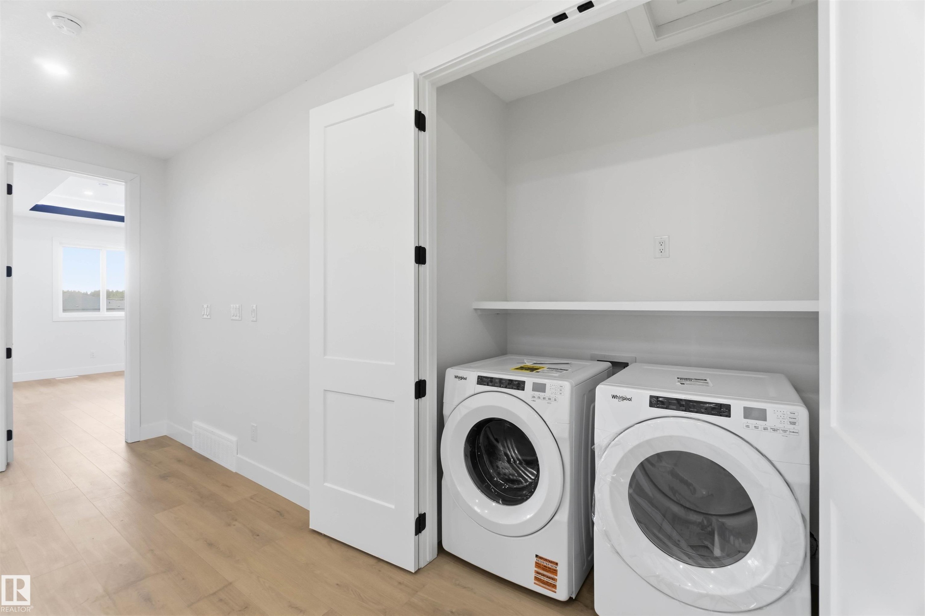 Dedicated laundry closet featuring a built-in shelf, white walls, and wood-finish flooring - 417 Pine Point(E), Leduc, AB - Indoor Photo Showing Laundry Room