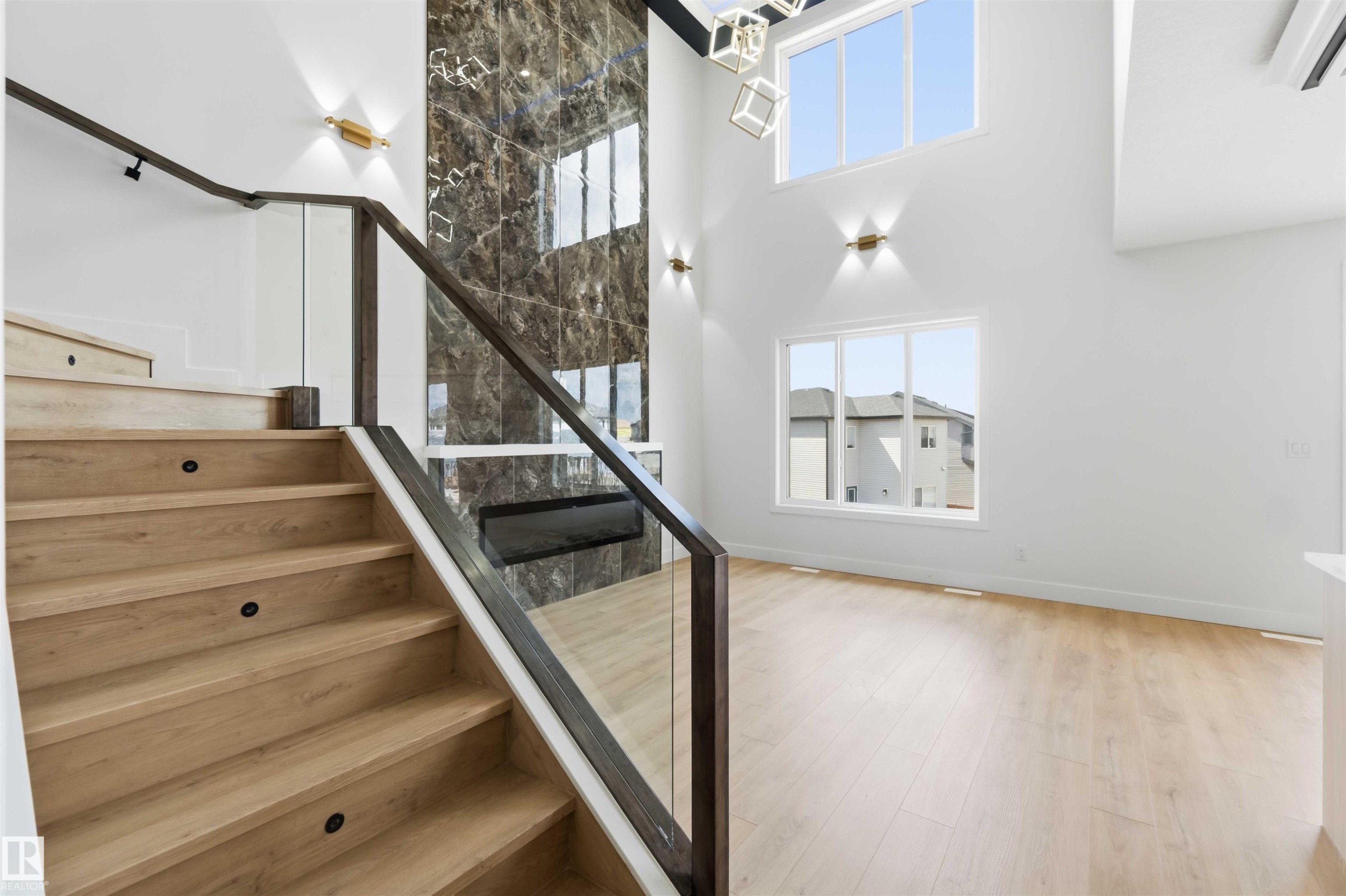 Bright interior featuring a grand staircase with wood treads and a glass railing - 417 Pine Point(E), Leduc, AB - Indoor Photo Showing Other Room