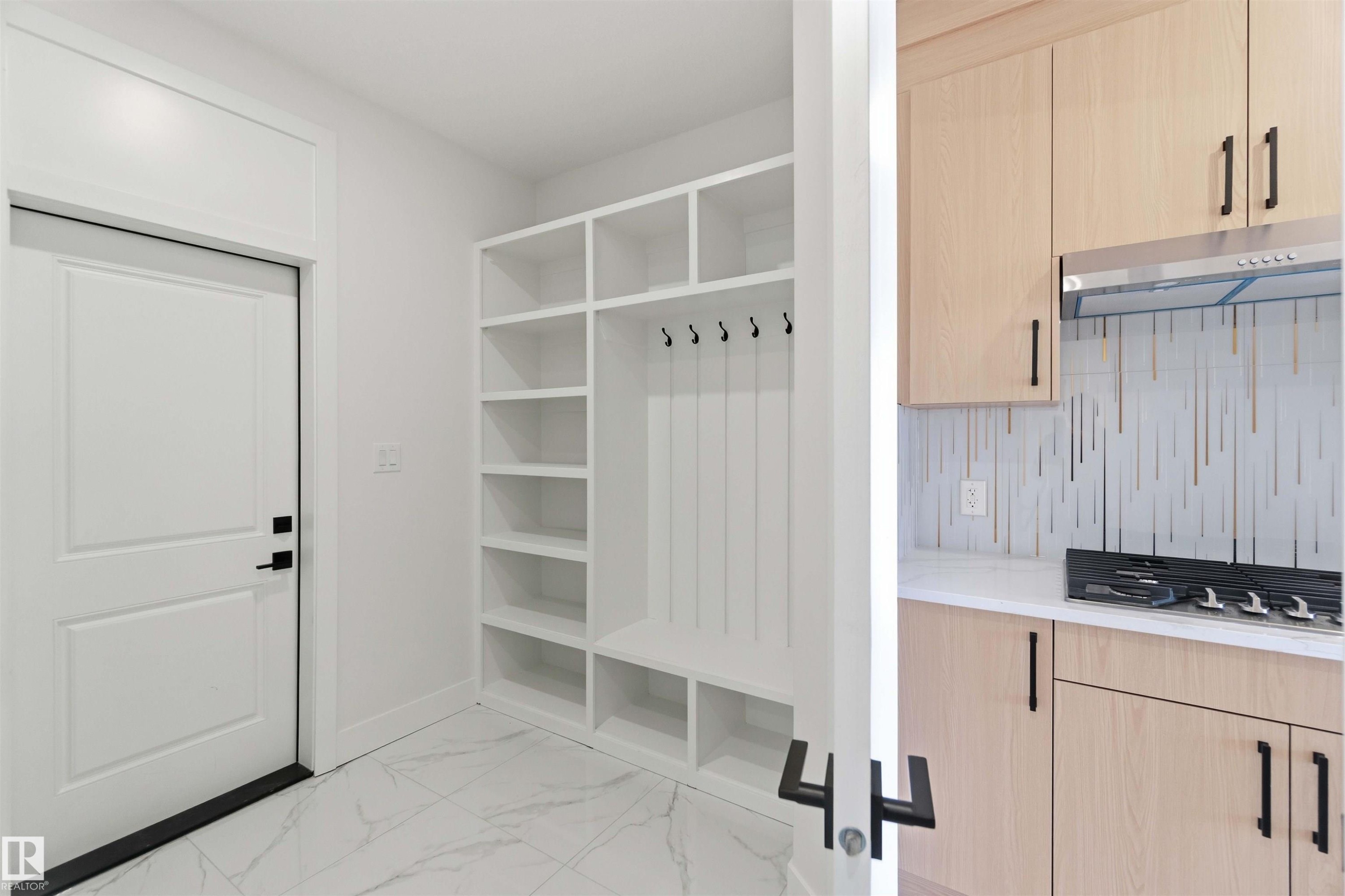 Entryway featuring a white paneled door with matte black hardware, built-in white storage shelving, and white marble-look tile flooring - 415 Pine Point(E), Leduc, AB - Indoor