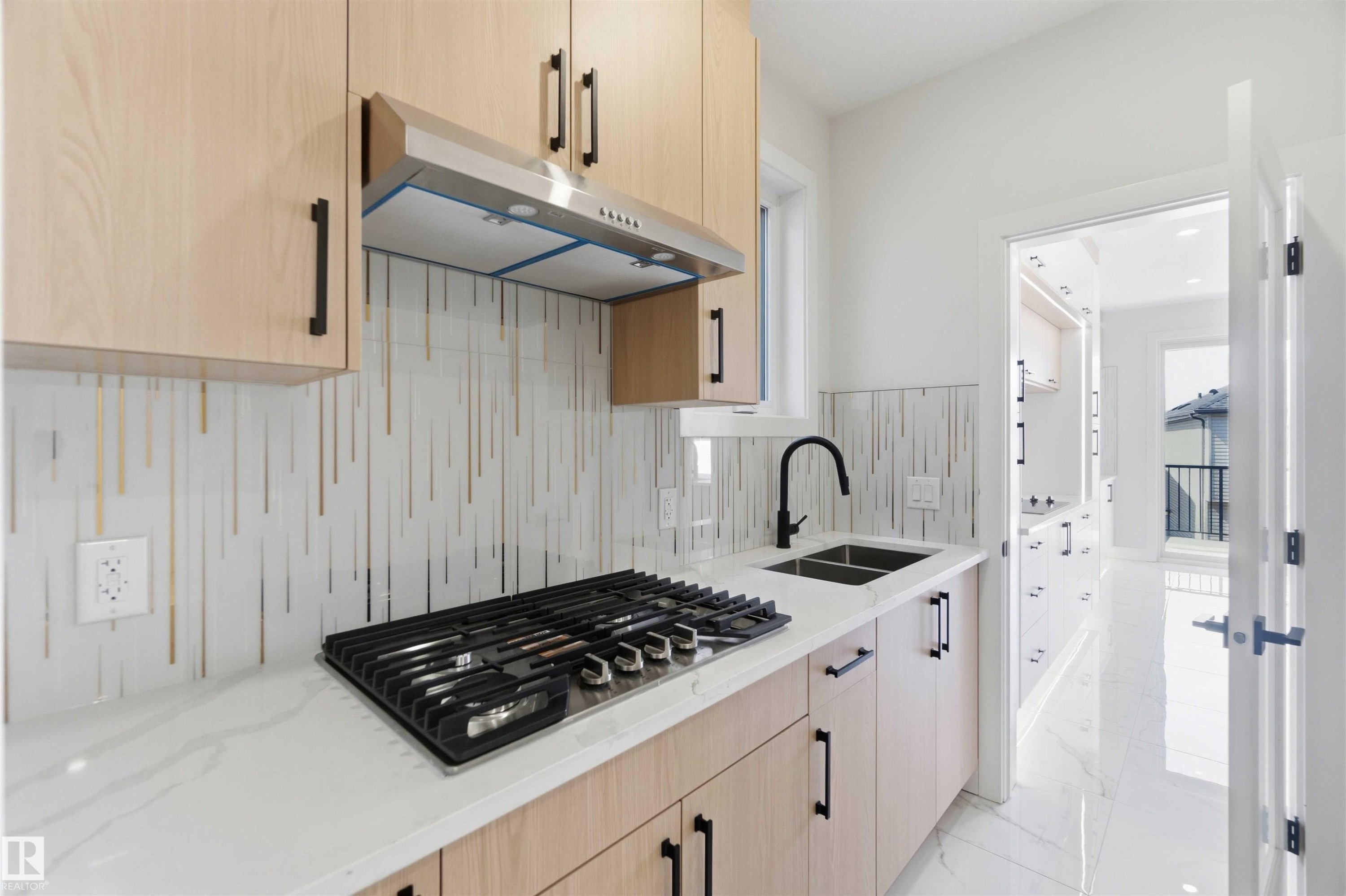 Modern kitchen featuring light wood-finish cabinetry with matte black hardware, a gas cooktop, and a stainless steel range hood - 415 Pine Point(E), Leduc, AB - Indoor Photo Showing Kitchen With Double Sink With Upgraded Kitchen