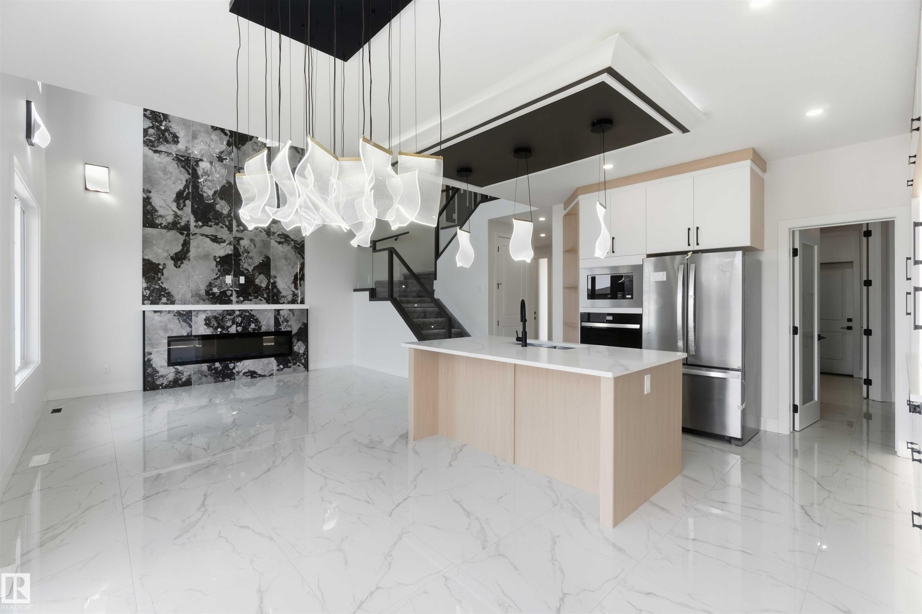 Open-concept interior featuring large format marble-look tile flooring, a modern kitchen island with a built-in sink, stainless steel appliances, a striking fireplace with a stone surround, and an elegant staircase with glass railings - 415 Pine Point(E), Leduc, AB - Indoor Photo Showing Kitchen