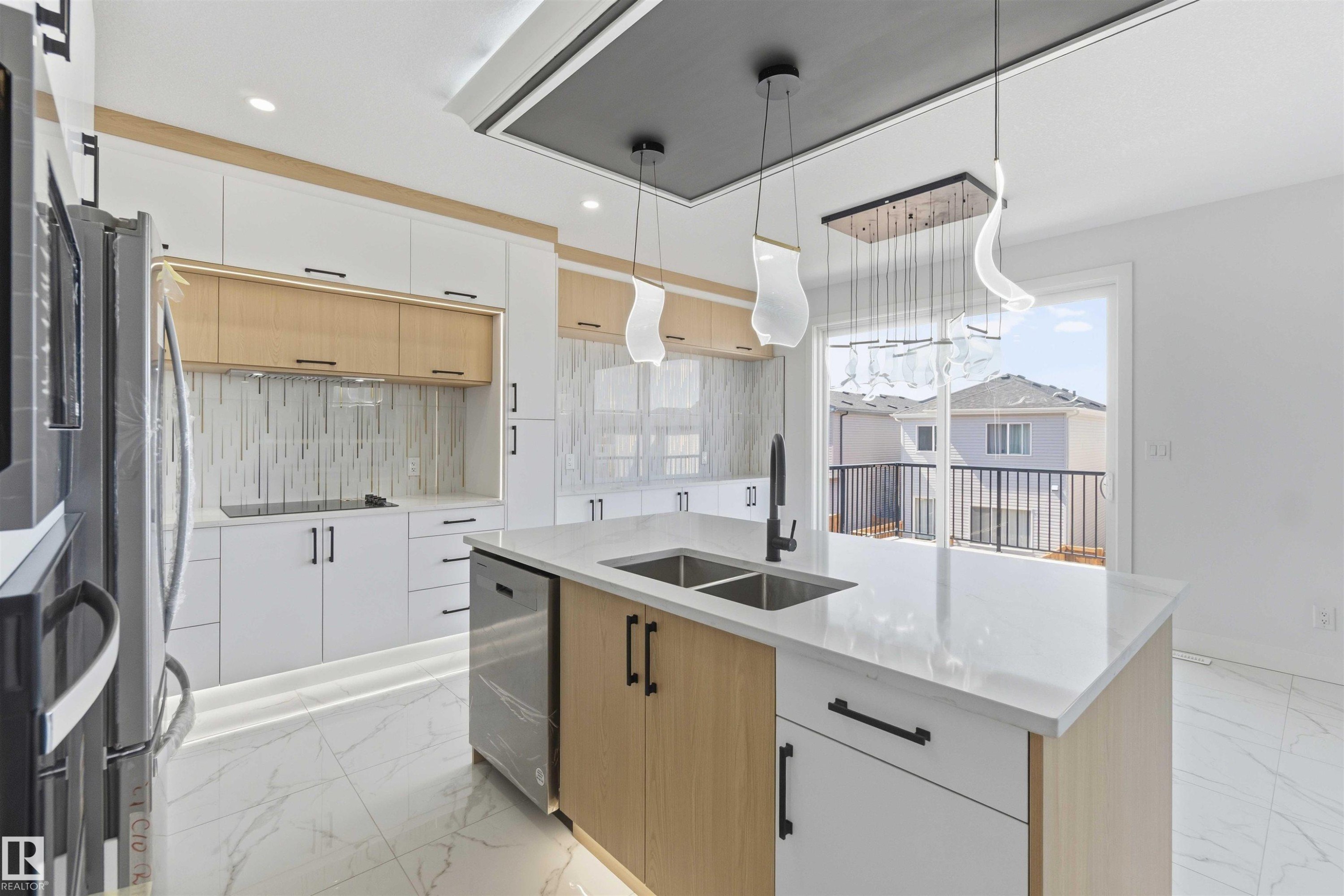 Modern kitchen featuring a large central island with an undermount double sink, sleek white cabinetry, wood-finish accent cabinets, and a tile backsplash - 415 Pine Point(E), Leduc, AB - Indoor Photo Showing Kitchen With Double Sink With Upgraded Kitchen