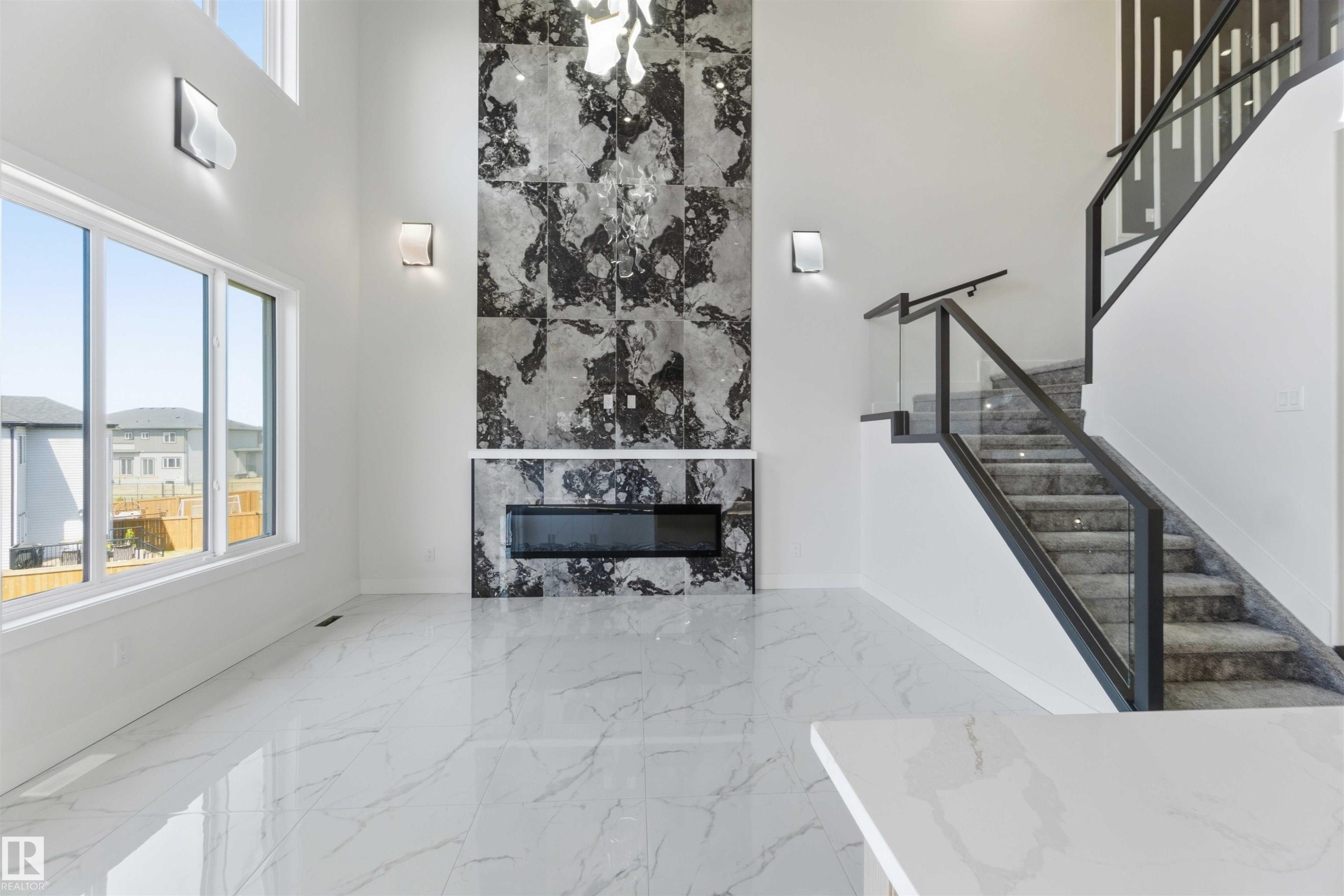 Two-story living area featuring a full-height fireplace with large format marble-look tile surround and a linear electric fireplace - 415 Pine Point(E), Leduc, AB - Indoor With Fireplace