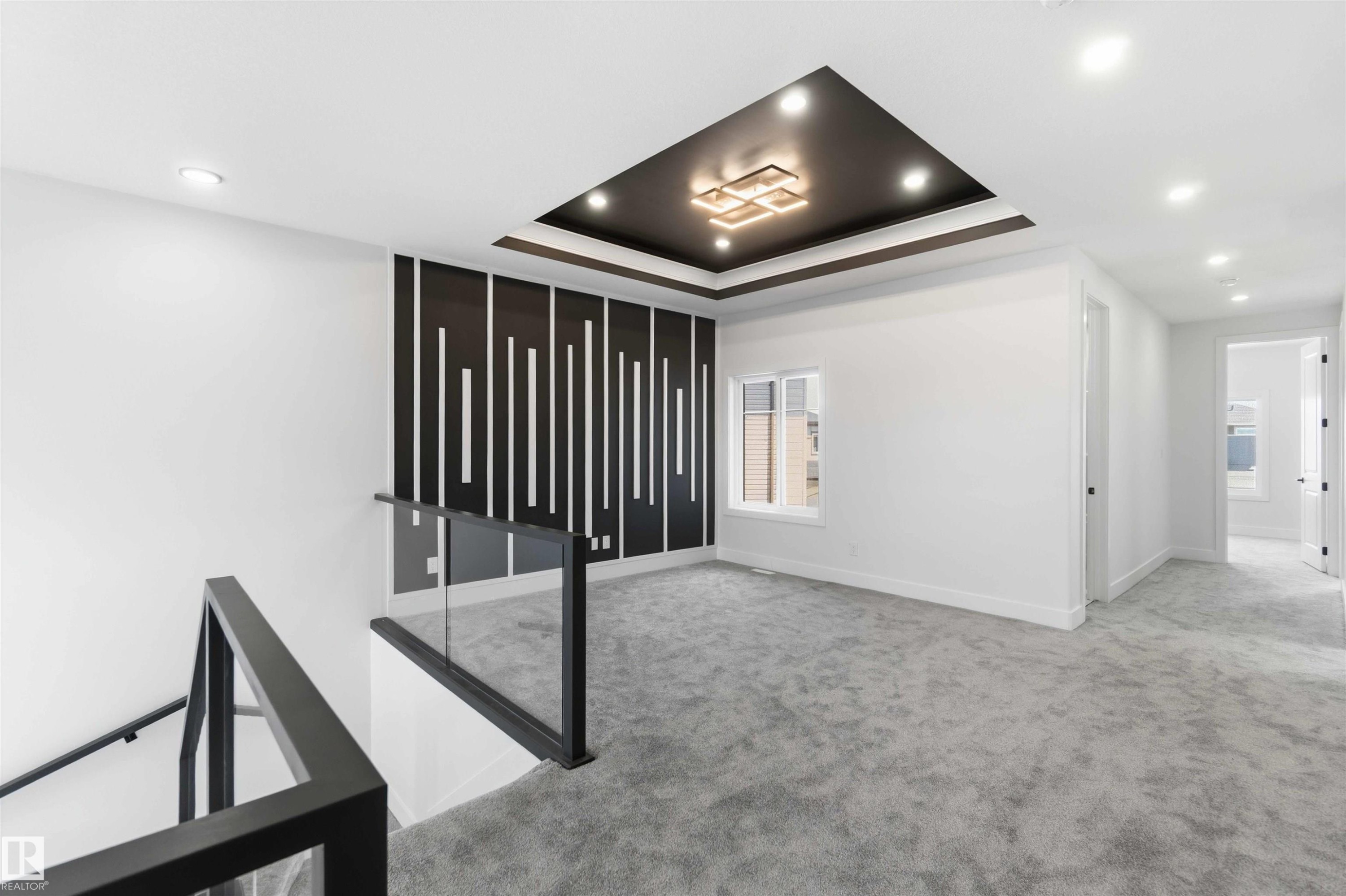 Open loft area featuring a tray ceiling with recessed lighting, a modern chandelier, and patterned accent wall - 415 Pine Point(E), Leduc, AB - Indoor Photo Showing Other Room