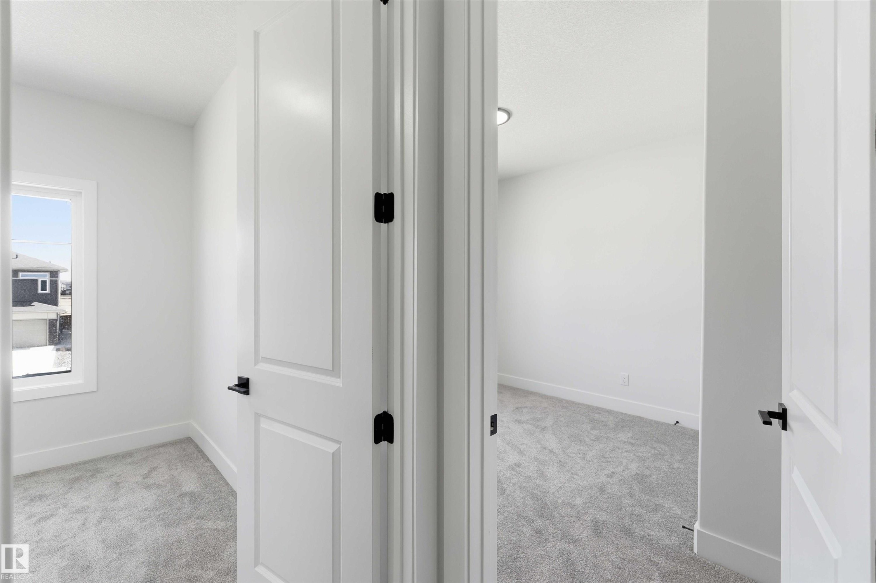 Two rooms featuring light gray carpeting, crisp white walls, and modern white paneled doors with matte black hardware - 415 Pine Point(E), Leduc, AB - Indoor Photo Showing Other Room