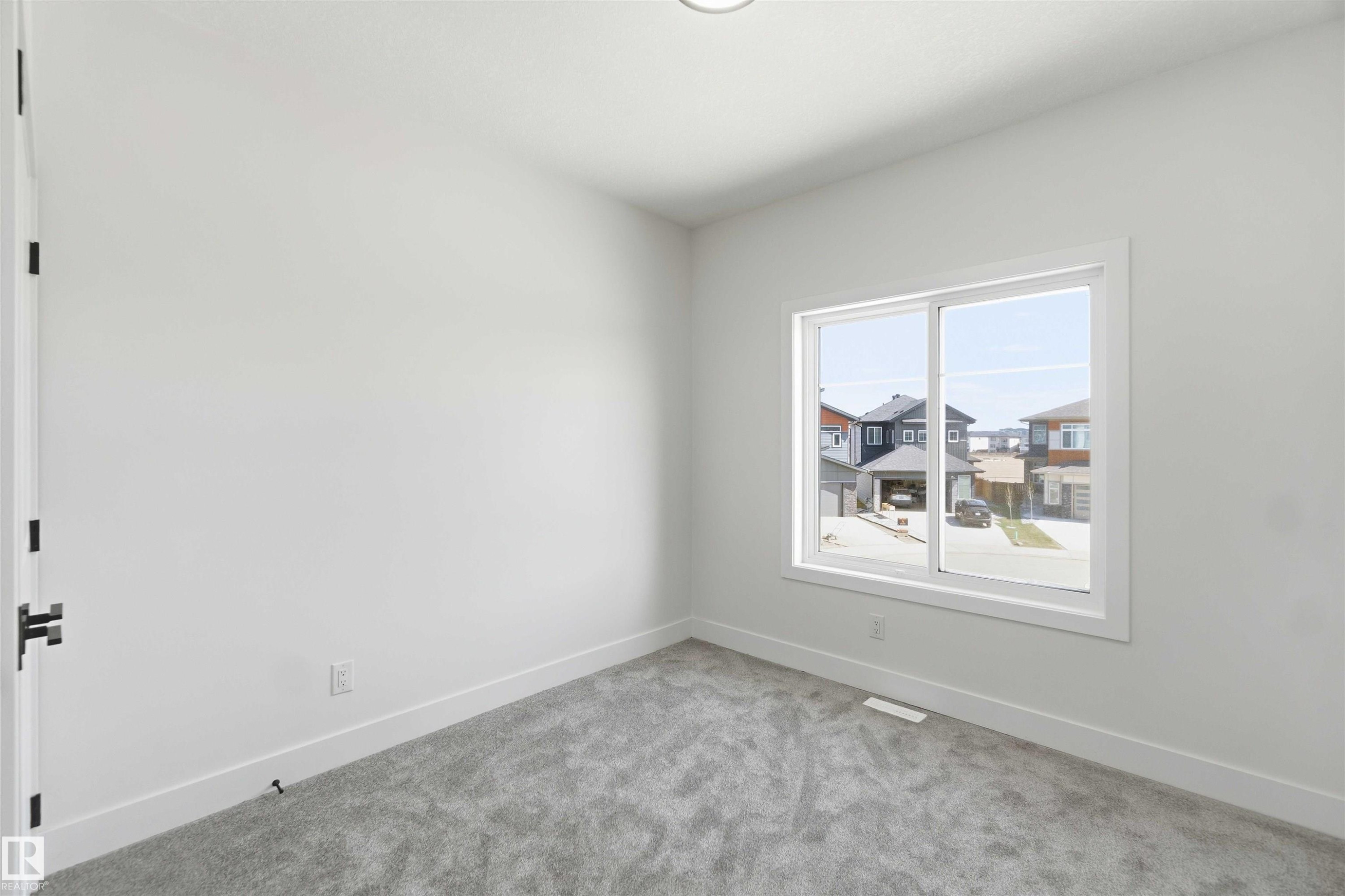 Bright interior space featuring a large window, light gray carpeting, crisp white walls, white trim, and a modern ceiling light fixture - 415 Pine Point(E), Leduc, AB - Indoor Photo Showing Other Room