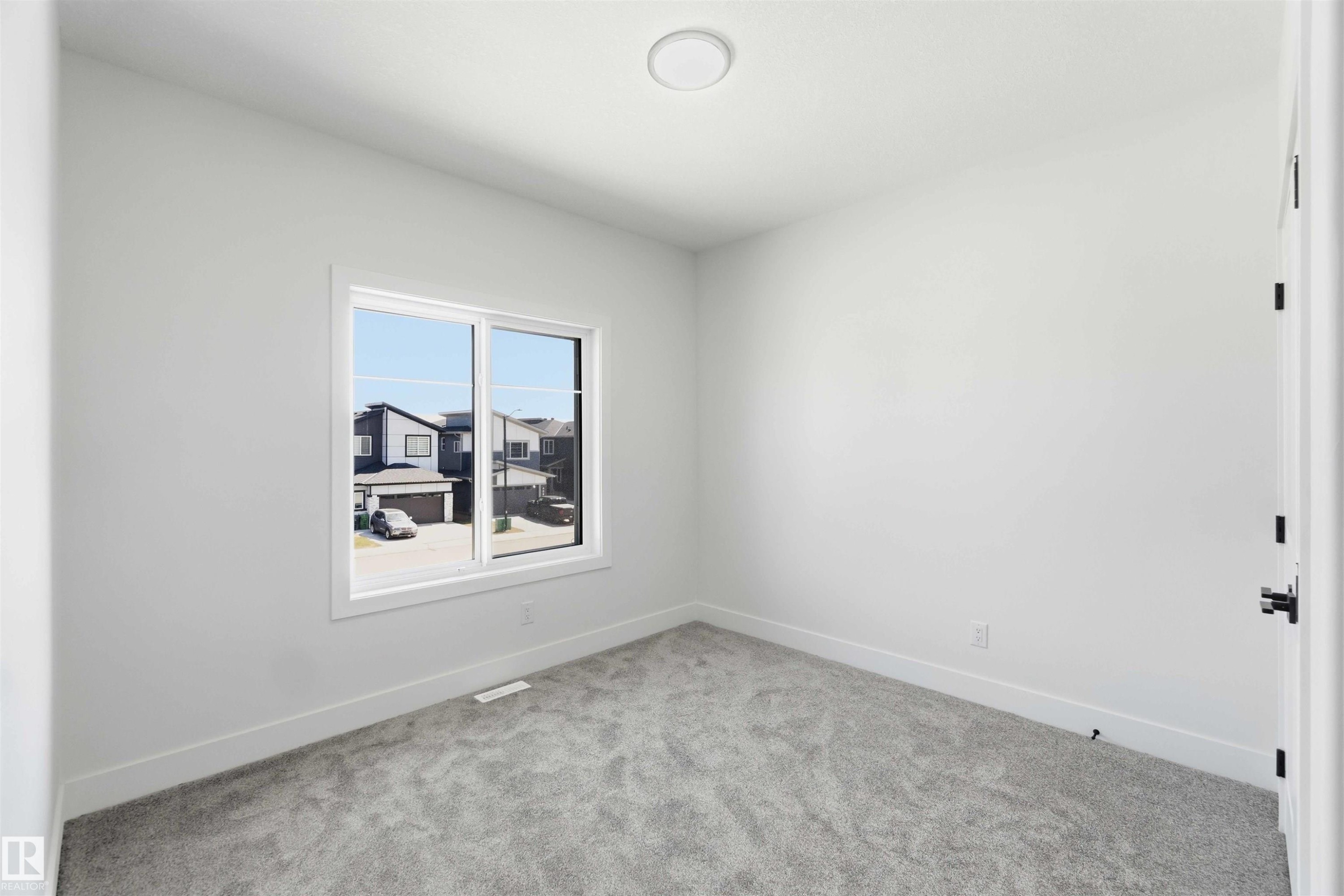 Bright interior space featuring a double-pane window, light gray carpet, white baseboards, and a circular flush-mount ceiling light - 415 Pine Point(E), Leduc, AB - Indoor Photo Showing Other Room