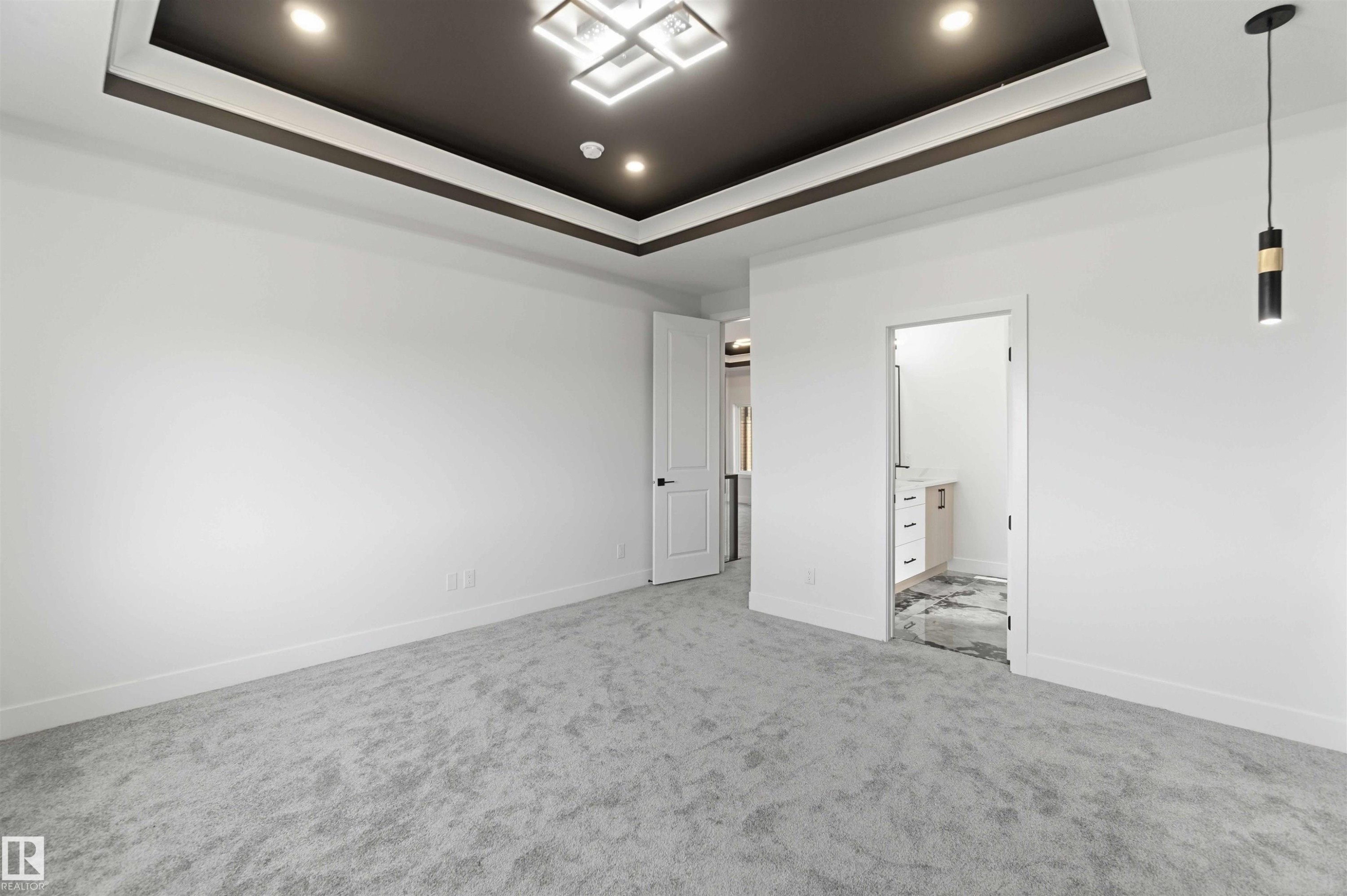 Spacious room featuring a tray ceiling with recessed lighting and a geometric chandelier, light gray carpeting, and white walls with thick baseboards - 415 Pine Point(E), Leduc, AB - Indoor Photo Showing Other Room