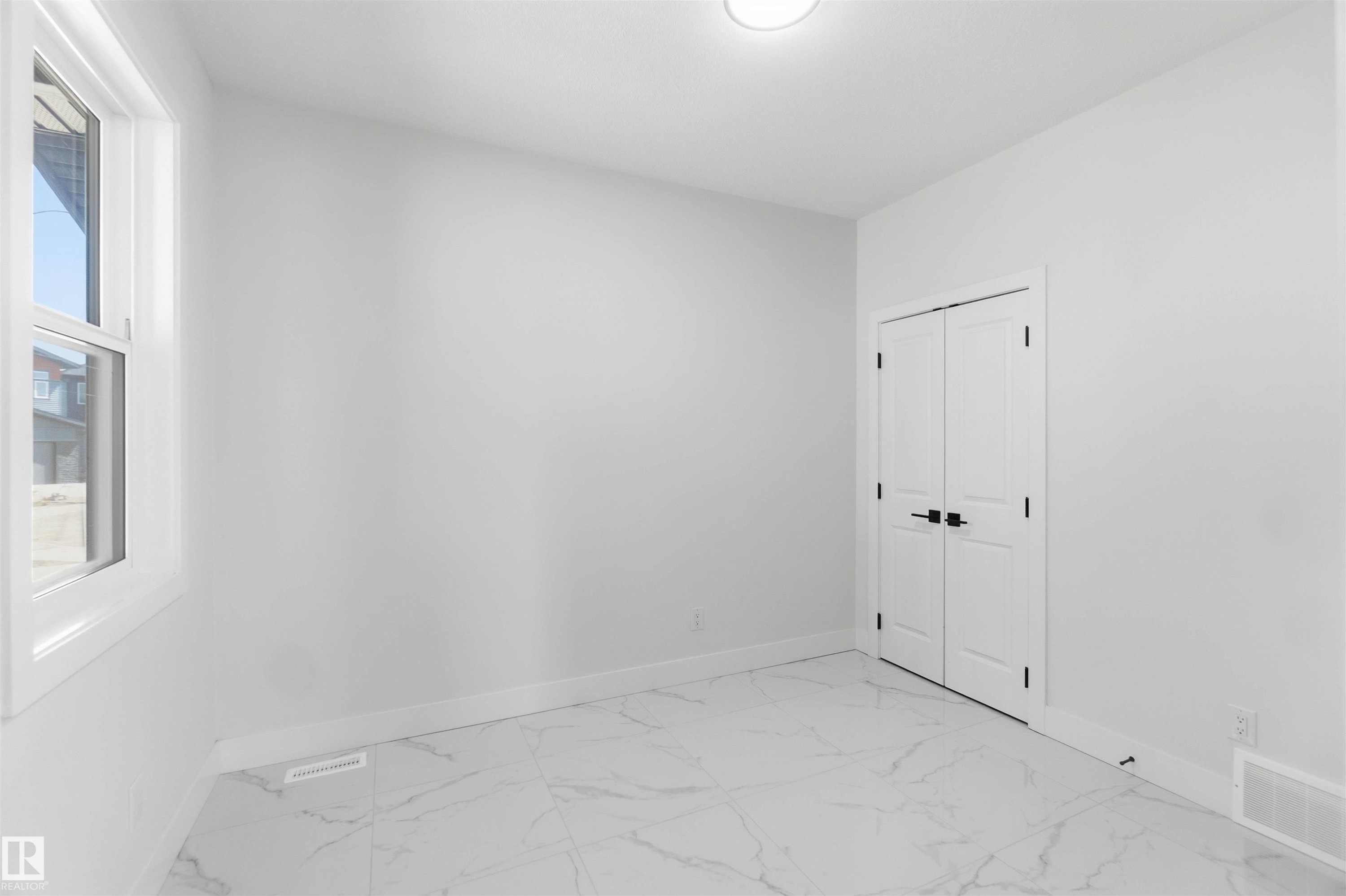 Bright room featuring white walls, large window, white trim, and white double doors with matte black hardware - 415 Pine Point(E), Leduc, AB - Indoor Photo Showing Other Room