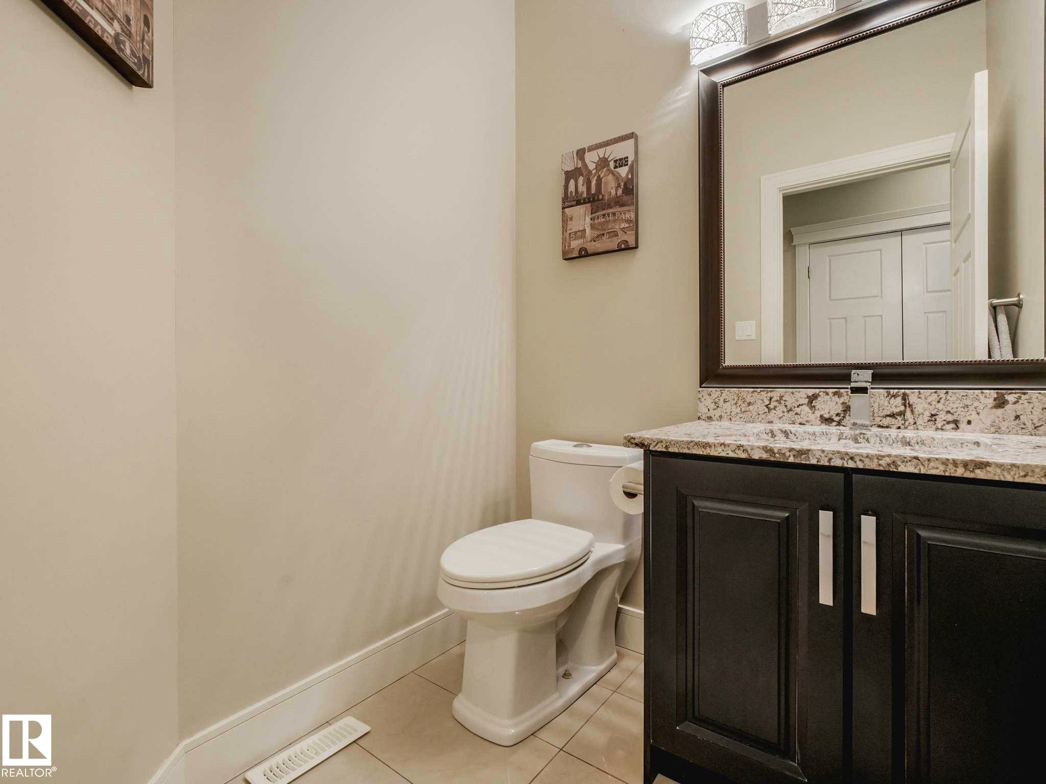 Bathroom featuring a dark wood vanity with a light speckled countertop, framed mirror, and a three-light vanity fixture - 16251 135 Street Nw, Edmonton, AB - Indoor Photo Showing Bathroom