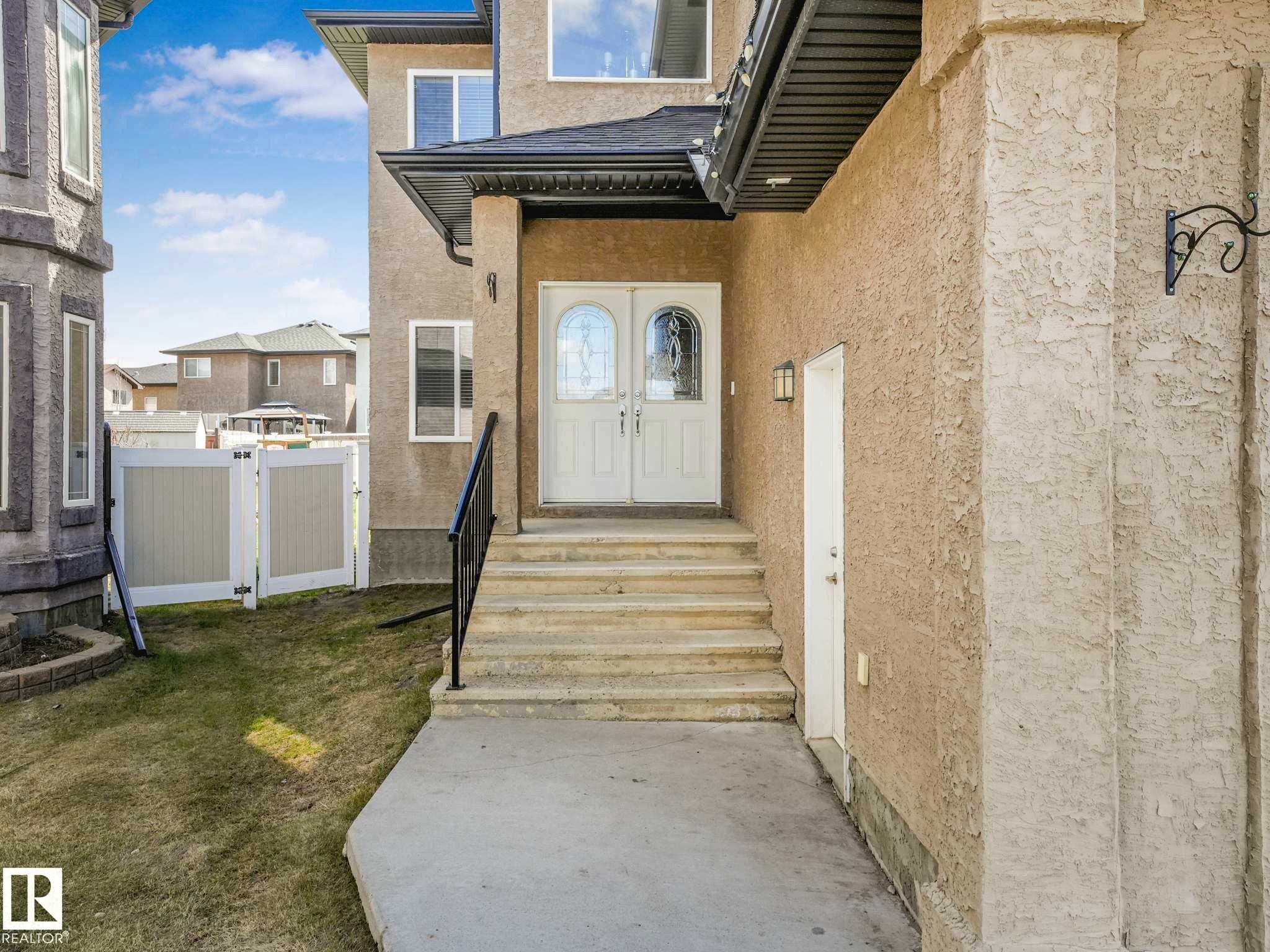 Stucco exterior featuring a double-door entry with arched glass inserts, concrete steps with a black metal handrail, and white framed windows - 16251 135 Street Nw, Edmonton, AB - Outdoor