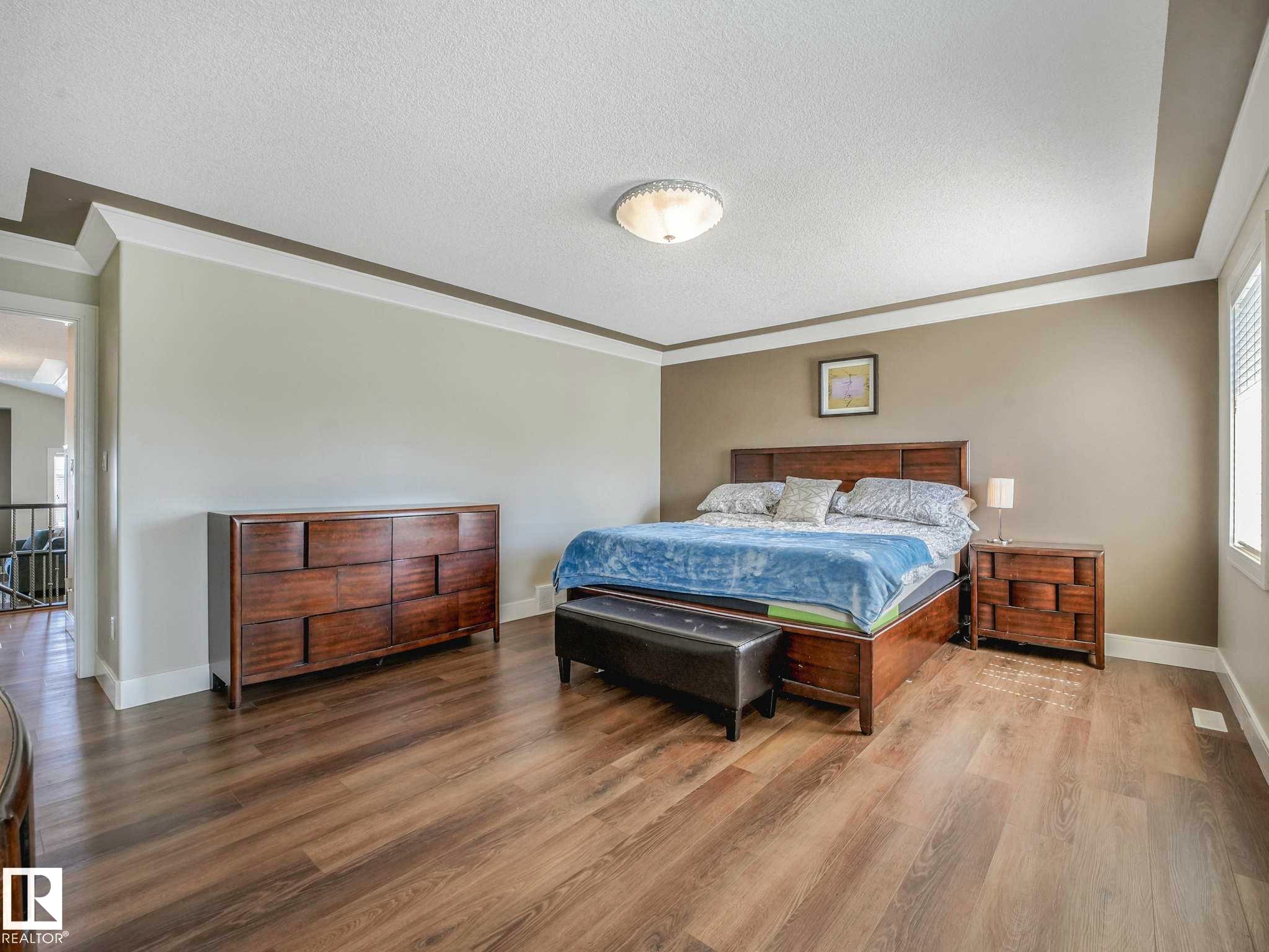 Spacious room featuring wood-finish flooring, a tray ceiling with crown molding, and neutral wall tones - 16251 135 Street Nw, Edmonton, AB - Indoor Photo Showing Bedroom
