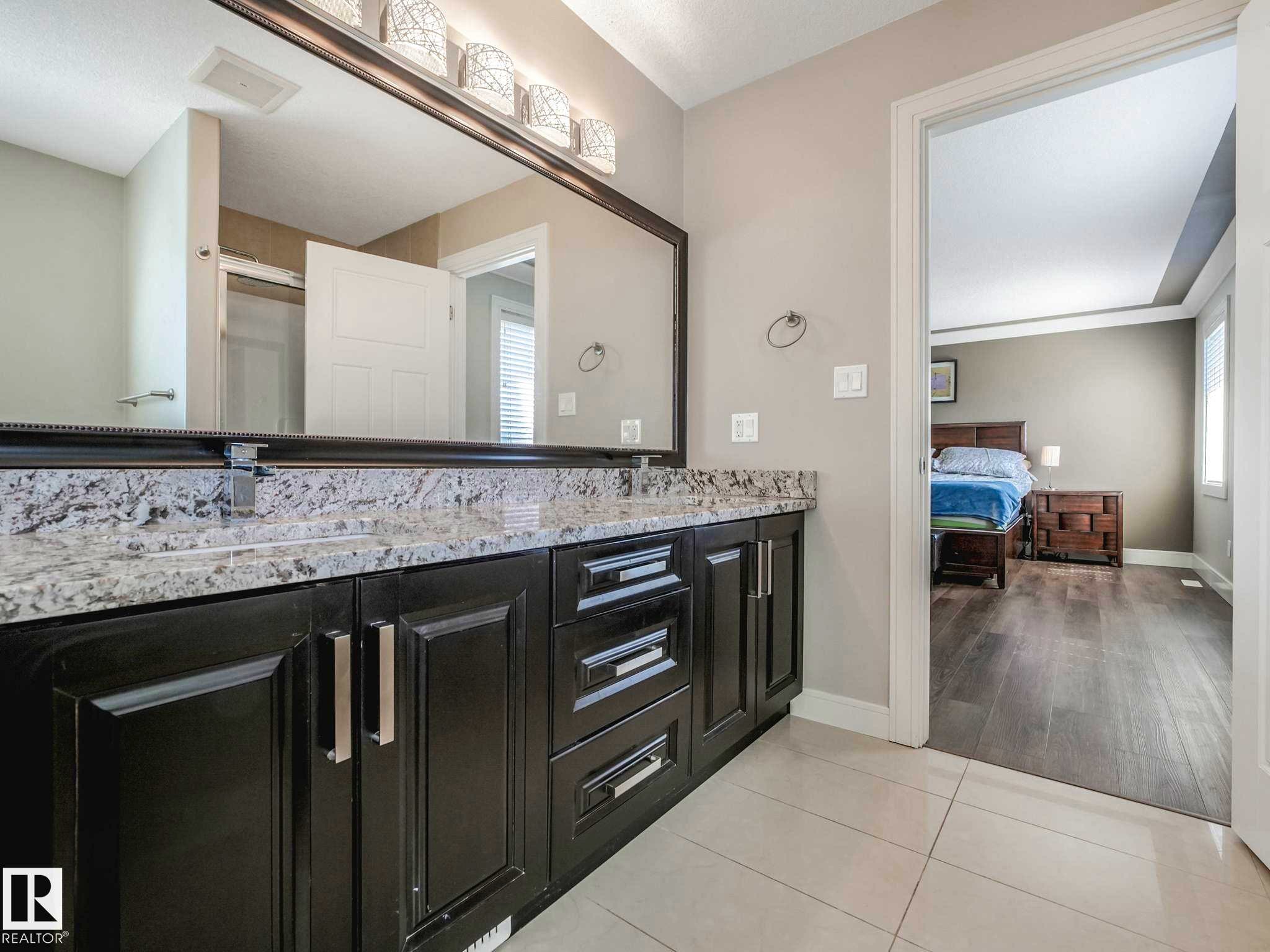 Bathroom vanity featuring a dual sink design with a granite countertop, dark wood-finish cabinetry, and brushed nickel hardware - 16251 135 Street Nw, Edmonton, AB - Indoor Photo Showing Bathroom