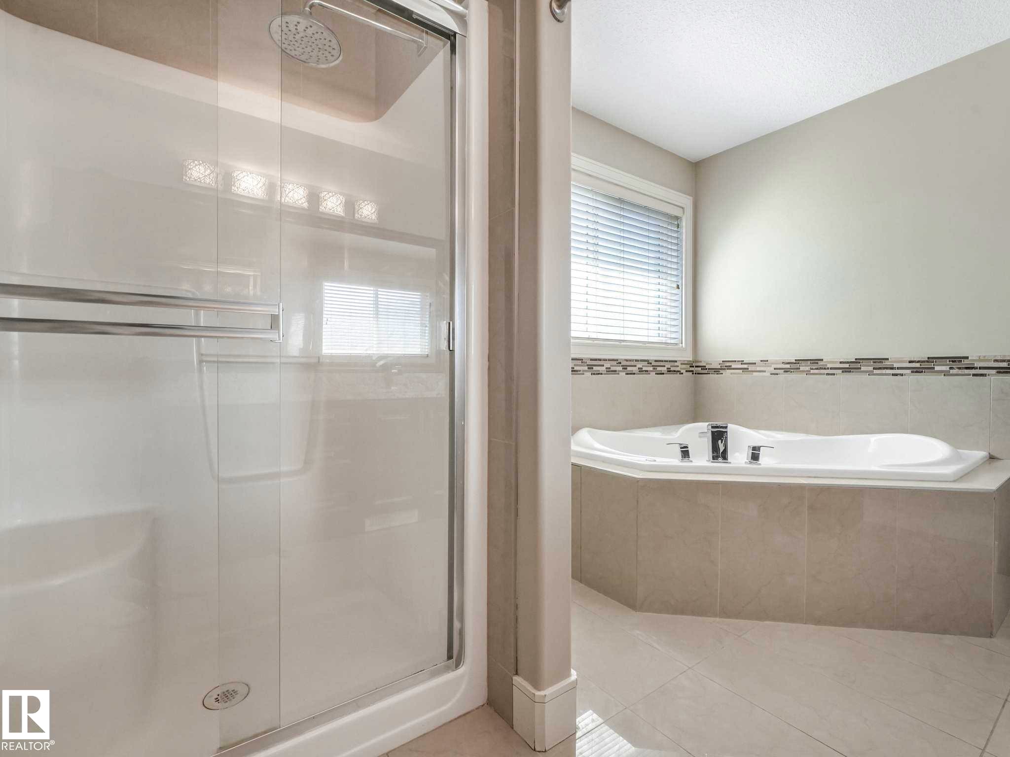 Bathroom featuring a glass-enclosed shower, a built-in corner soaking tub, a tiled tub surround, and a decorative tile accent band - 16251 135 Street Nw, Edmonton, AB - Indoor Photo Showing Bathroom