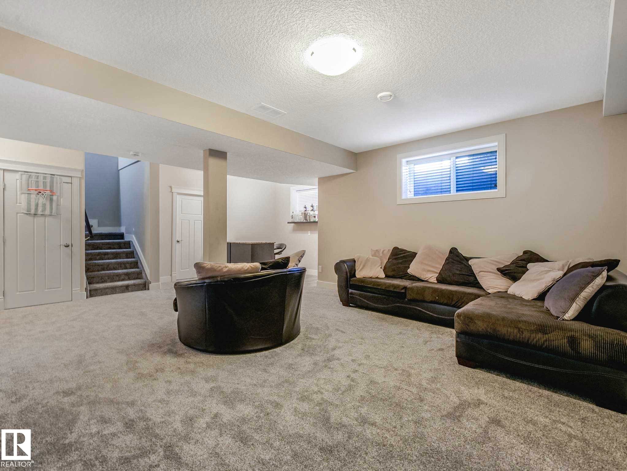 Spacious carpeted room featuring a white ceiling, recessed lighting, and a horizontal window with blinds - 16251 135 Street Nw, Edmonton, AB - Indoor