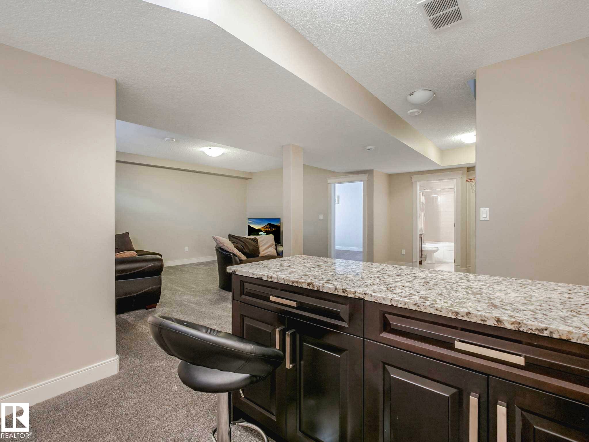 Entertainment space featuring a dark wood-finish cabinet island with a light speckled countertop, recessed lighting, and light gray carpeted flooring - 16251 135 Street Nw, Edmonton, AB - Indoor Photo Showing Other Room