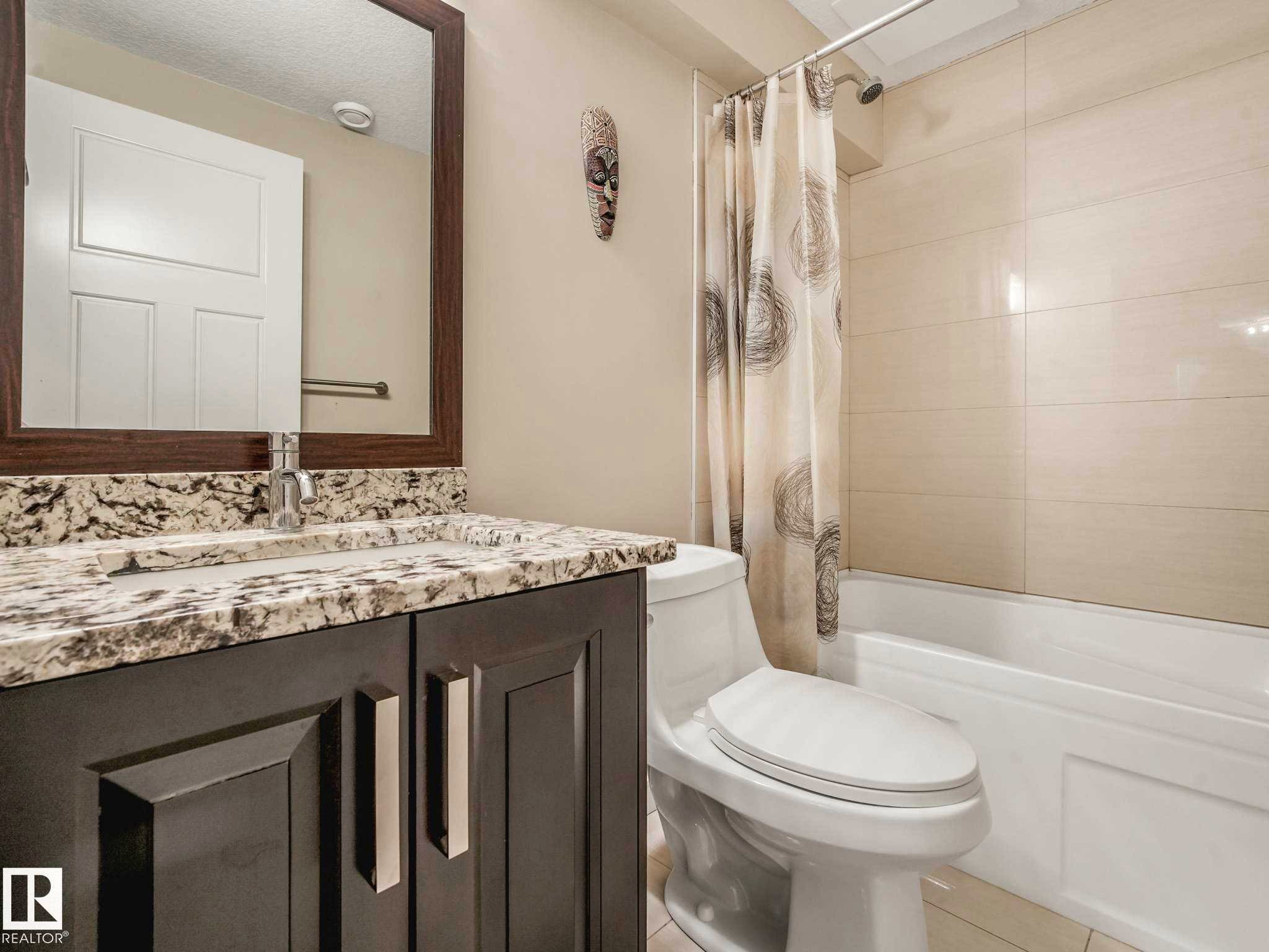 Bathroom featuring a vanity with a light-toned patterned countertop, a built-in sink with a chrome faucet, and a framed mirror - 16251 135 Street Nw, Edmonton, AB - Indoor Photo Showing Bathroom