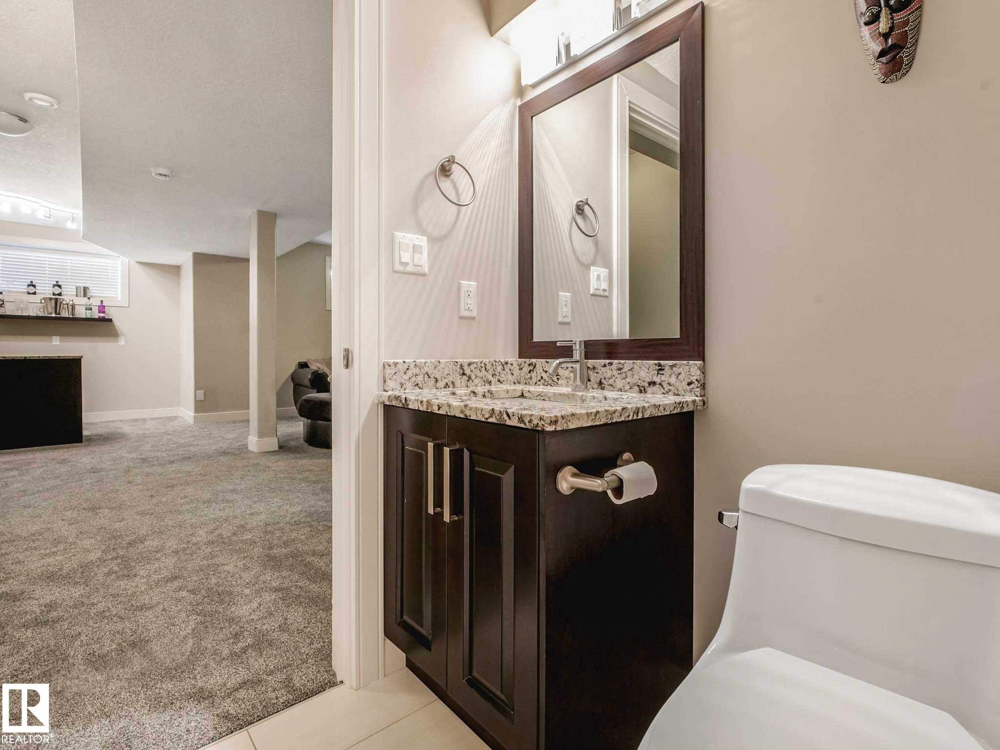 Bathroom vanity featuring a framed mirror, a granite-finish countertop, and dark wood-finish cabinetry - 16251 135 Street Nw, Edmonton, AB - Indoor Photo Showing Bathroom