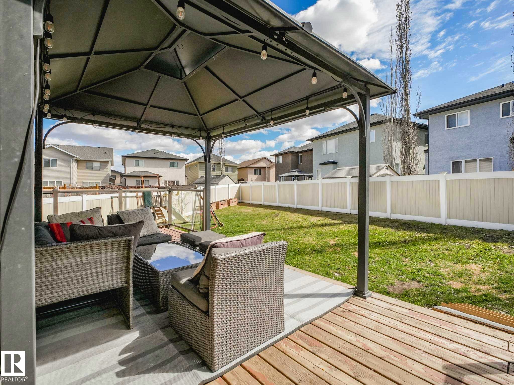 Expansive backyard featuring a gazebo-covered patio with string lights, a wood-finish deck, a concrete patio area, a manicured lawn, and privacy fencing - 16251 135 Street Nw, Edmonton, AB - Outdoor With Deck Patio Veranda