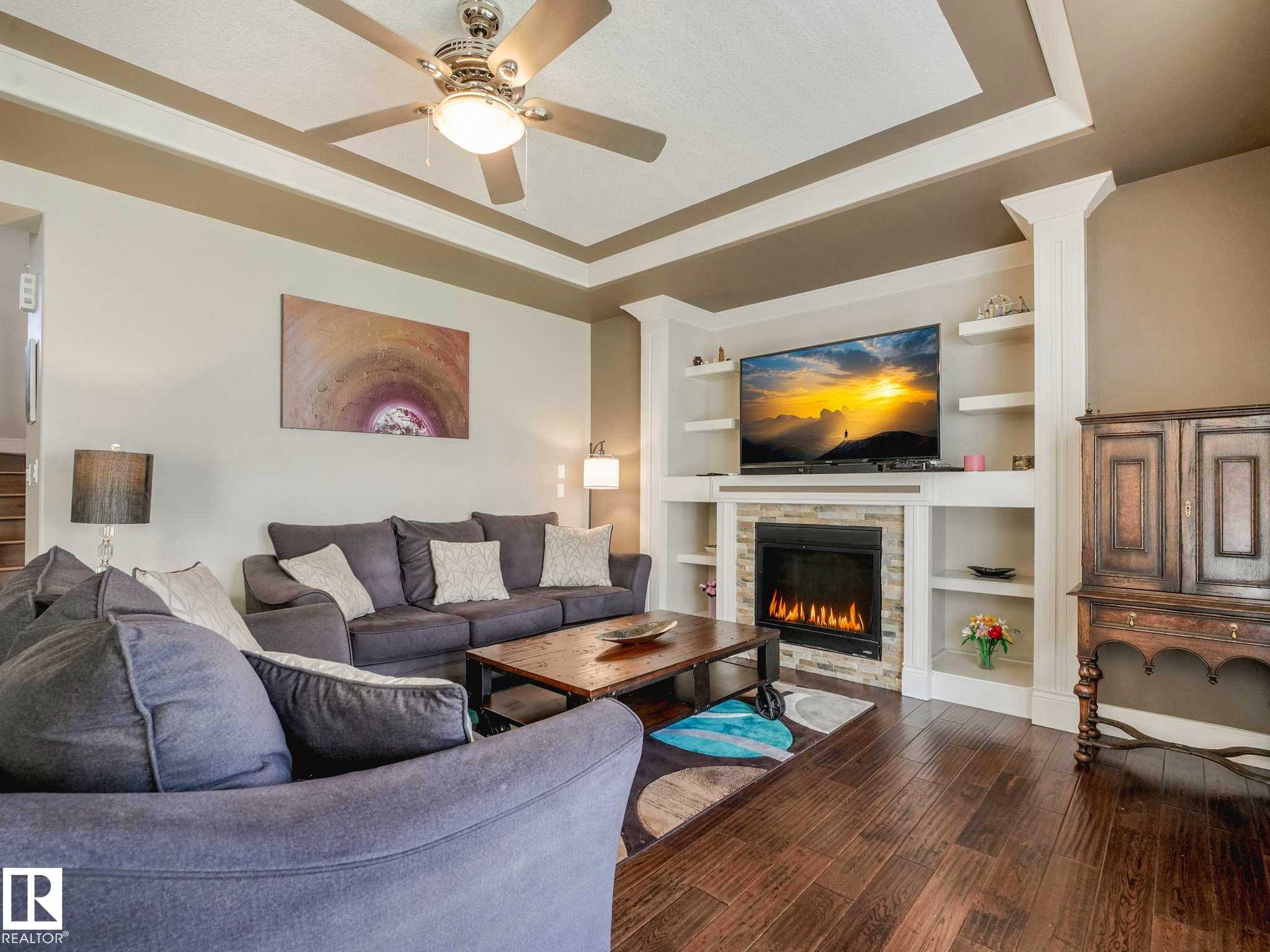 Living room featuring wood-finish flooring, a coffered ceiling with a ceiling fan, and a built-in media center with shelving - 16251 135 Street Nw, Edmonton, AB - Indoor Photo Showing Living Room With Fireplace