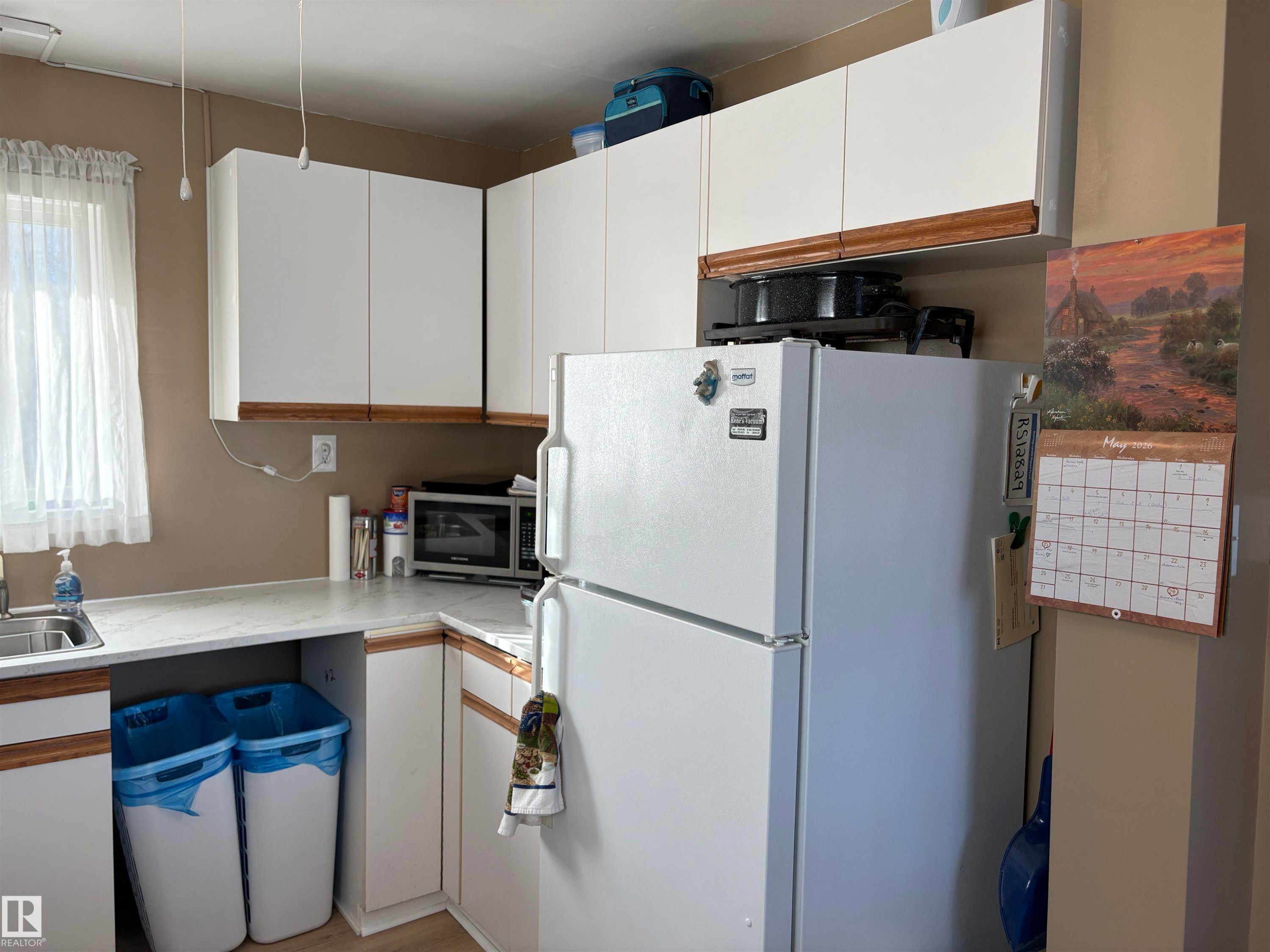 Kitchen featuring white cabinetry with wood-finish trim, a stainless steel sink, and white countertops - 410 Main St, Alcomdale, AB - Indoor Photo Showing Kitchen