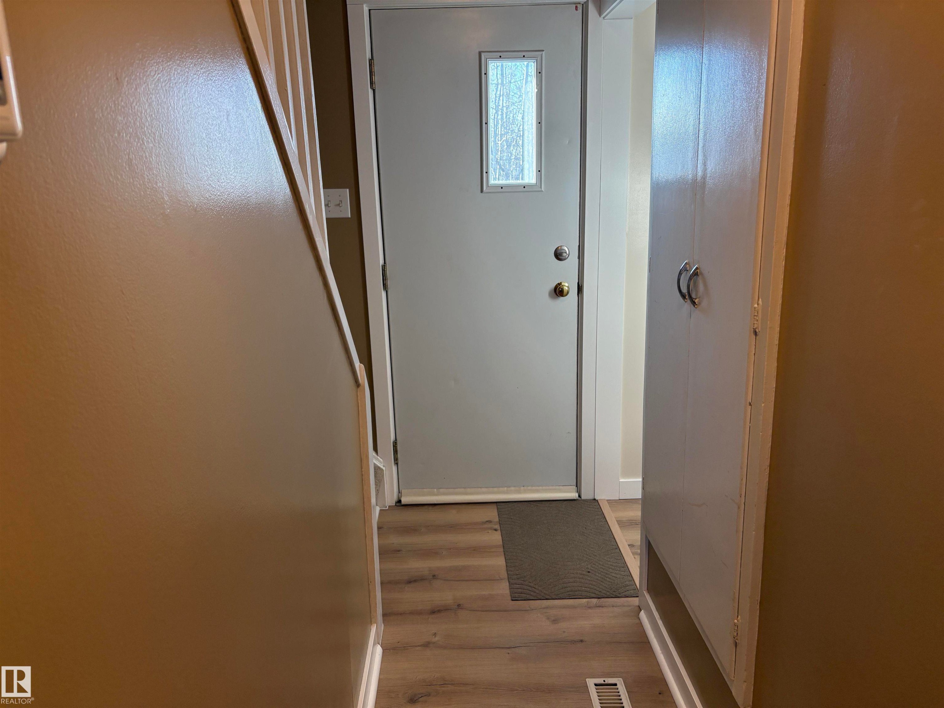 Entryway featuring a light gray door with a rectangular frosted glass insert, wood-finish flooring, and built-in white cabinetry with silver-tone hardware - 410 Main St, Alcomdale, AB - Indoor Photo Showing Other Room