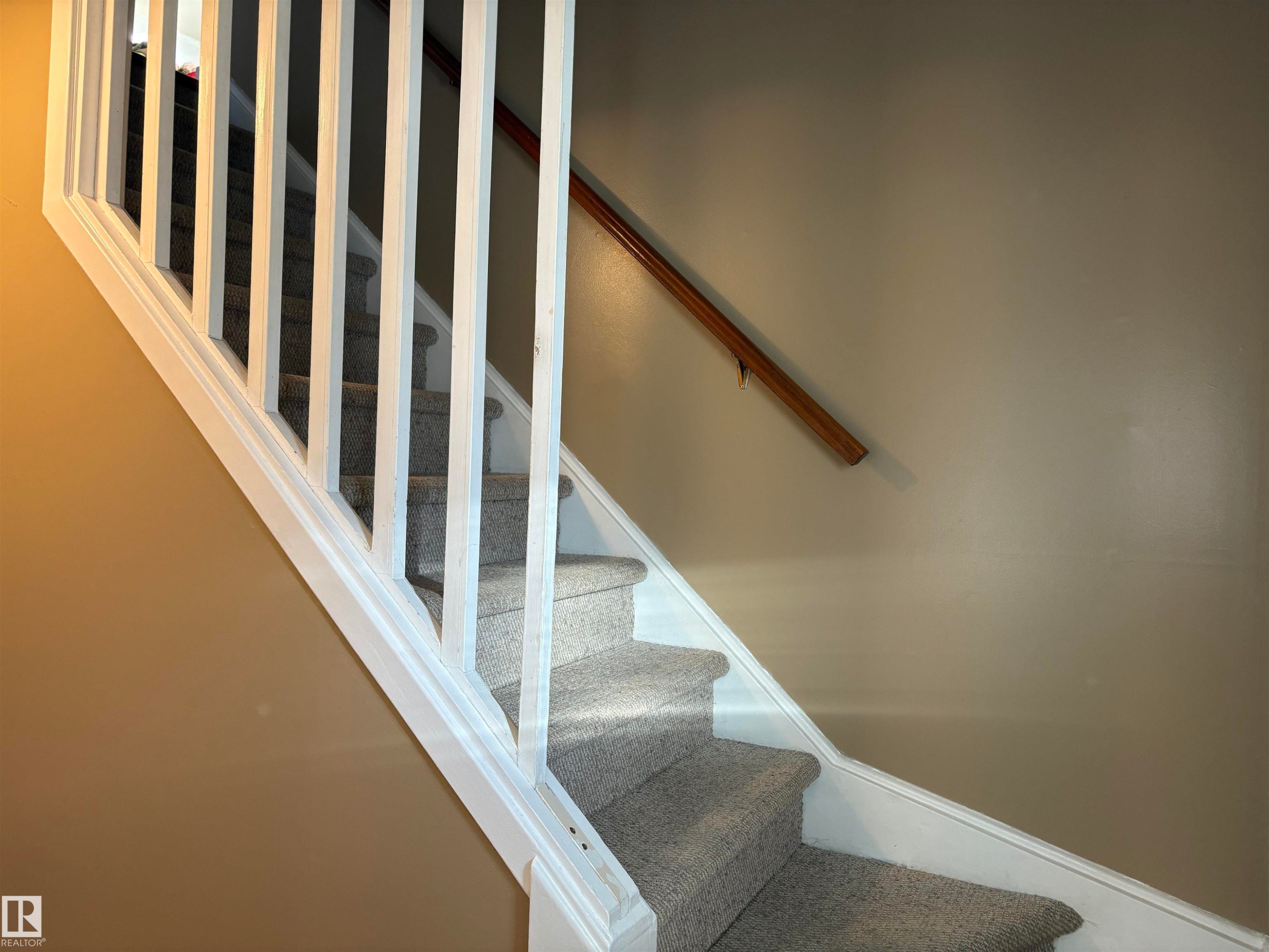Carpeted staircase featuring white balusters and a wood handrail - 410 Main St, Alcomdale, AB - Indoor Photo Showing Other Room