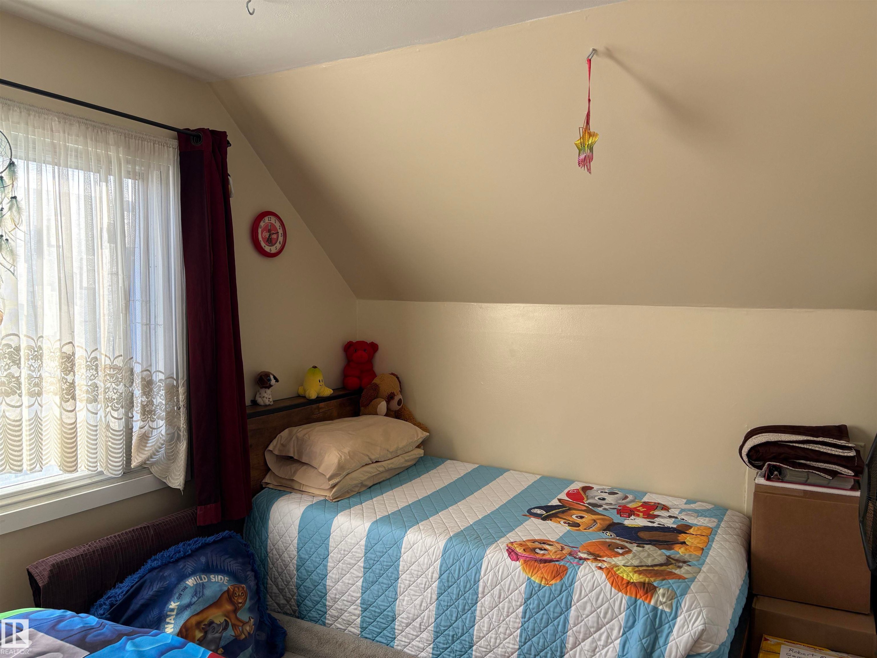 Sloped ceiling room featuring a window with sheer and solid drapes, and neutral wall tones - 410 Main St, Alcomdale, AB - Indoor Photo Showing Bedroom