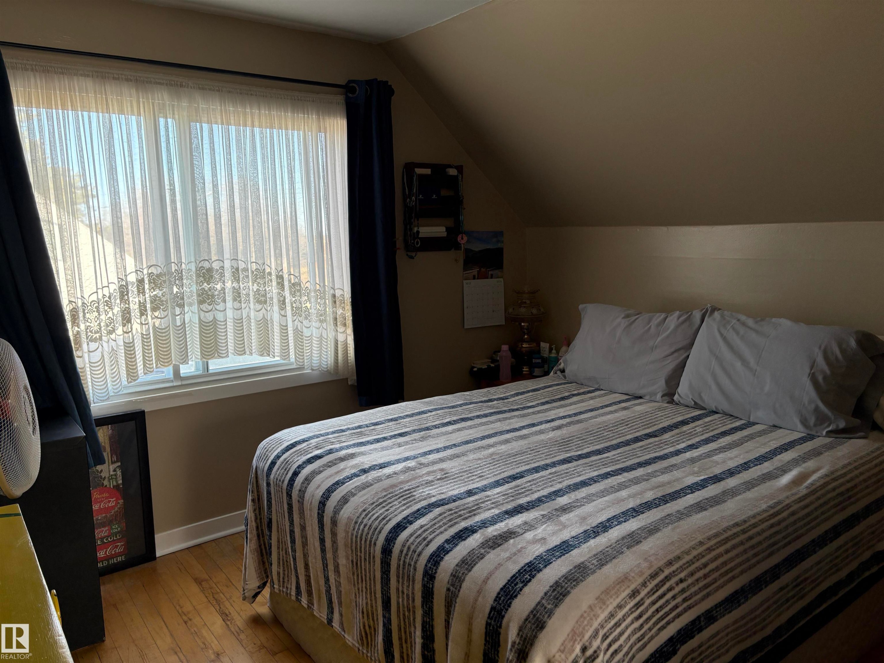 Attic bedroom featuring hardwood flooring and a window with sheer and blackout curtains - 410 Main St, Alcomdale, AB - Indoor Photo Showing Bedroom