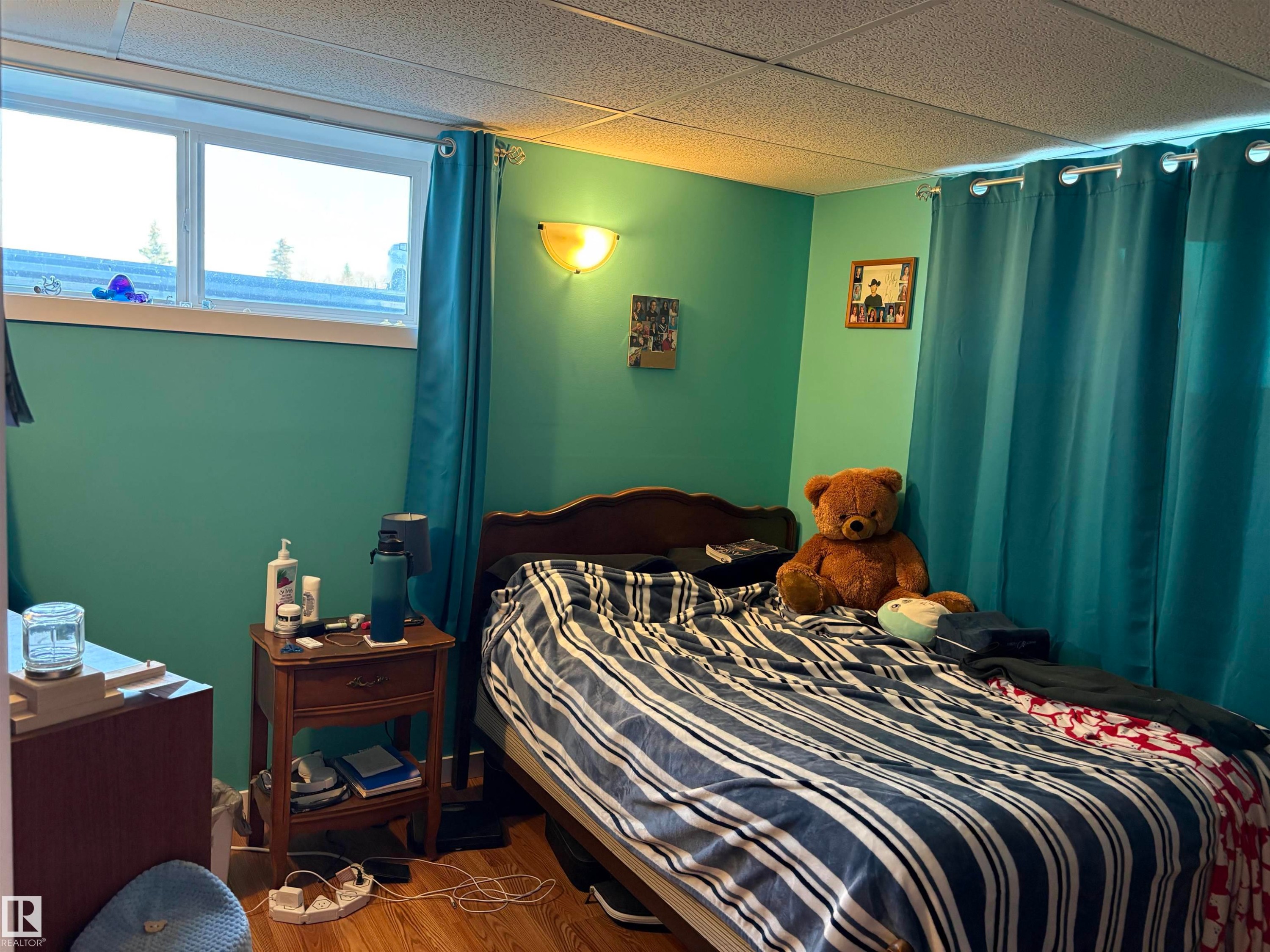 Room featuring a window with a white frame, wood-finish flooring, and a drop ceiling - 410 Main St, Alcomdale, AB - Indoor Photo Showing Bedroom