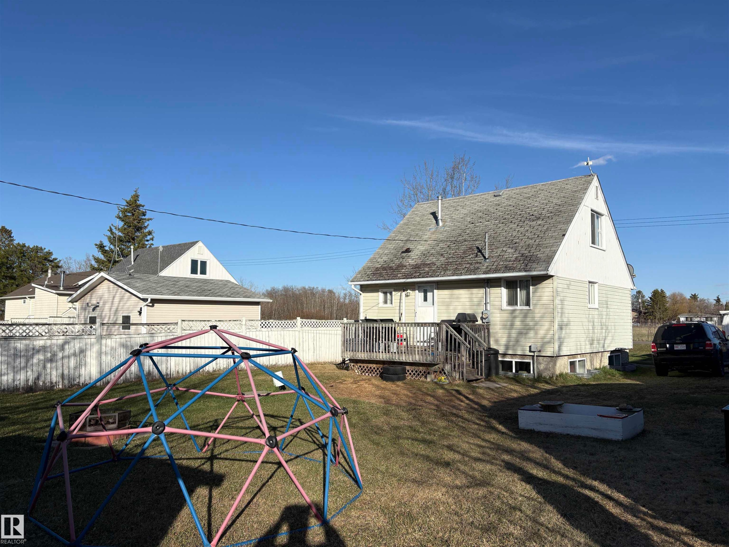 Expansive backyard featuring a partial privacy fence and an elevated wood deck - 410 Main St, Alcomdale, AB - Outdoor