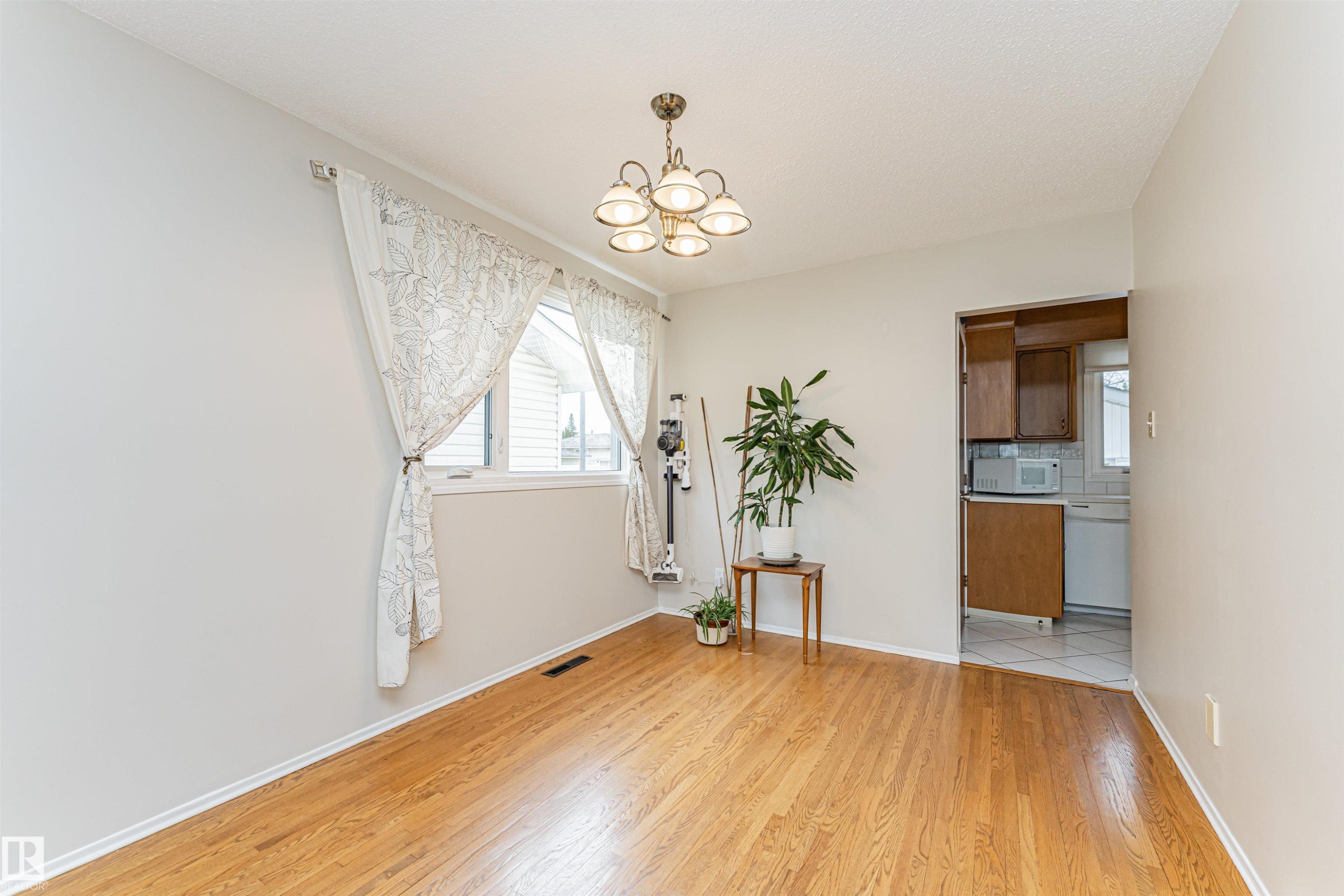 Hardwood-style flooring throughout, complemented by a central chandelier - 11423 50 Avenue, Edmonton, AB - Indoor Photo Showing Other Room