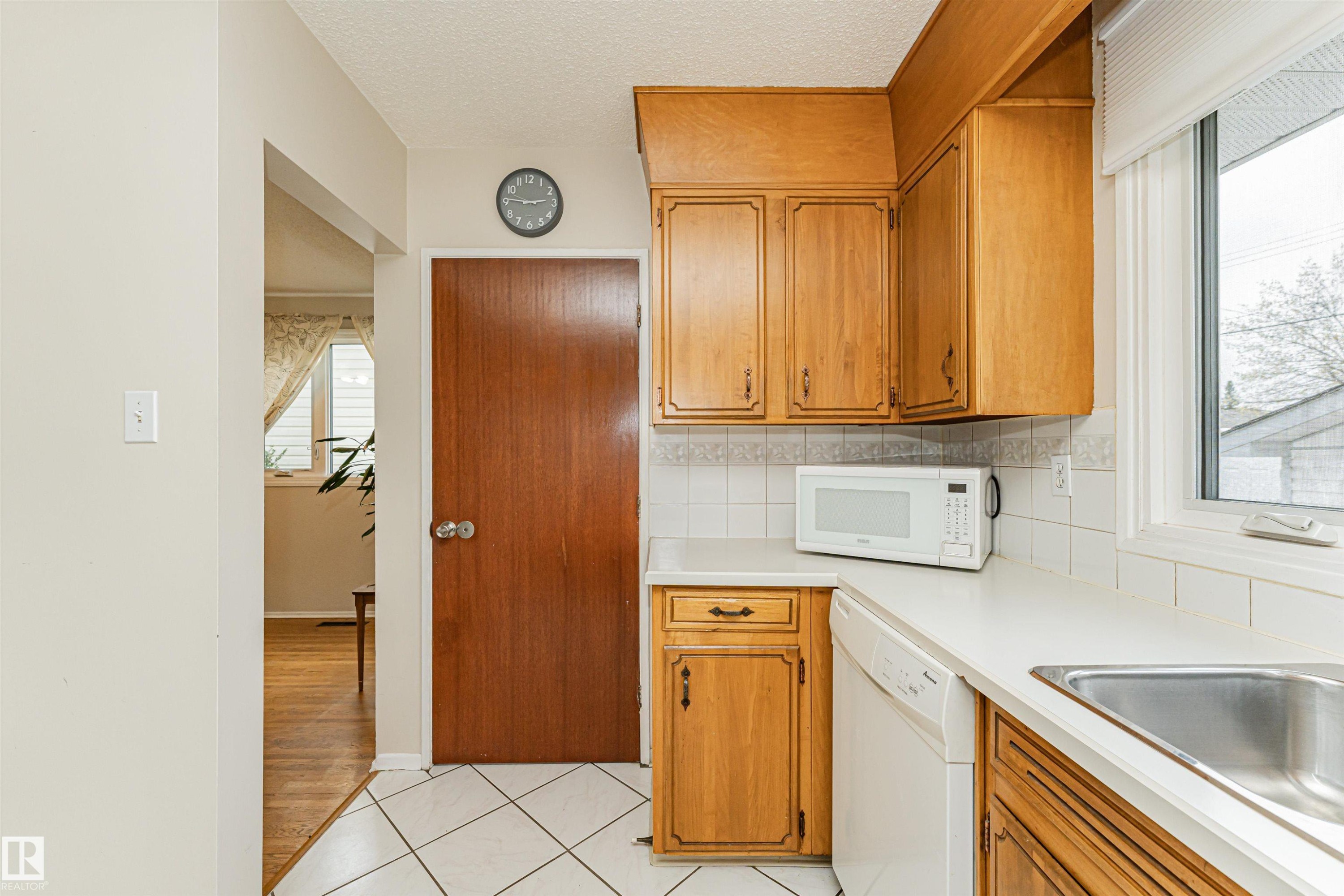Kitchen featuring wood cabinetry, white tiled backsplash, white countertops, and a stainless steel sink - 11423 50 Avenue, Edmonton, AB - Indoor Photo Showing Kitchen