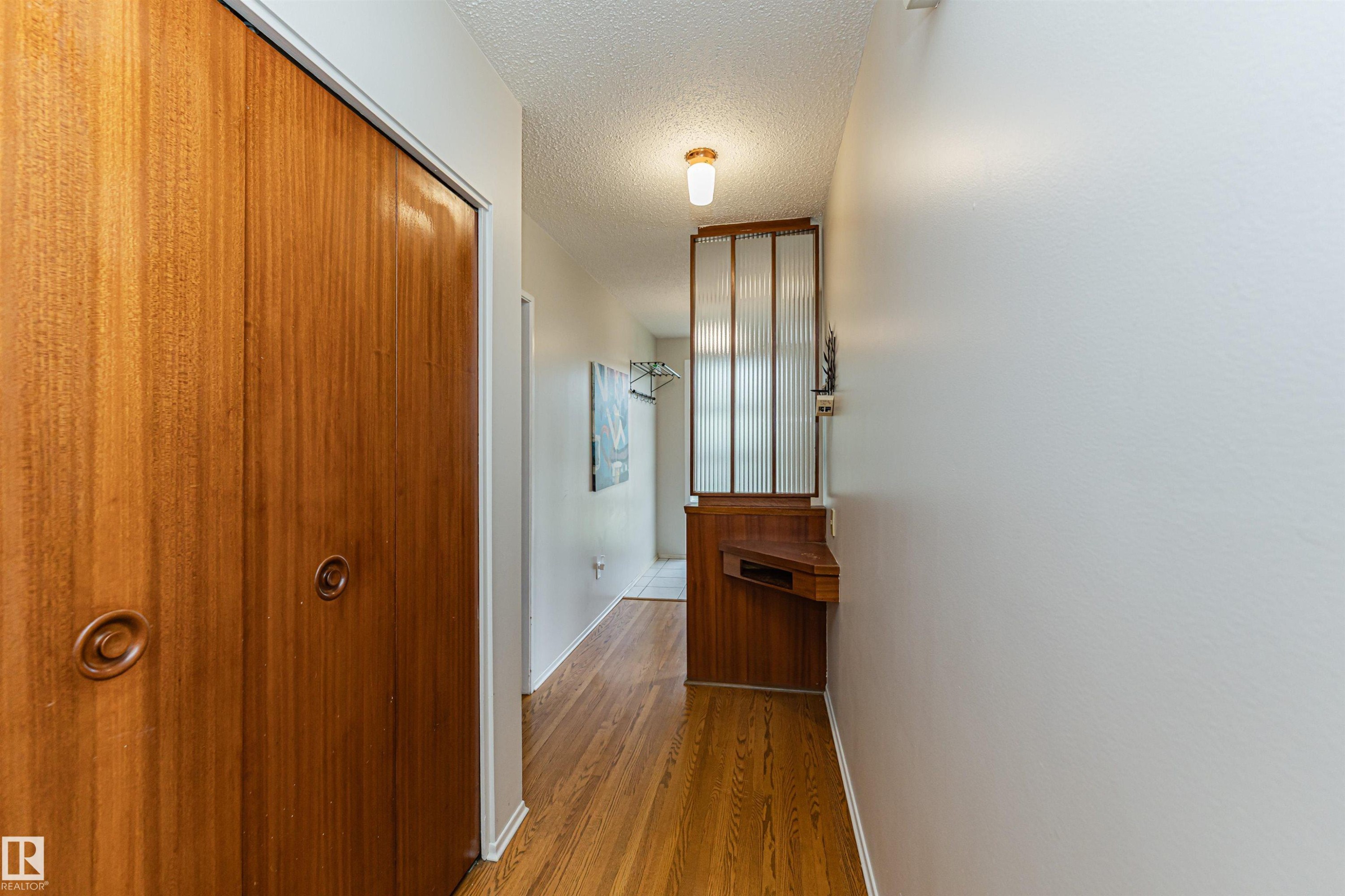 Hallway featuring wood-finish flooring, built-in storage with fluted glass paneling, and a flush-mount ceiling light fixture - 11423 50 Avenue, Edmonton, AB - Indoor Photo Showing Other Room
