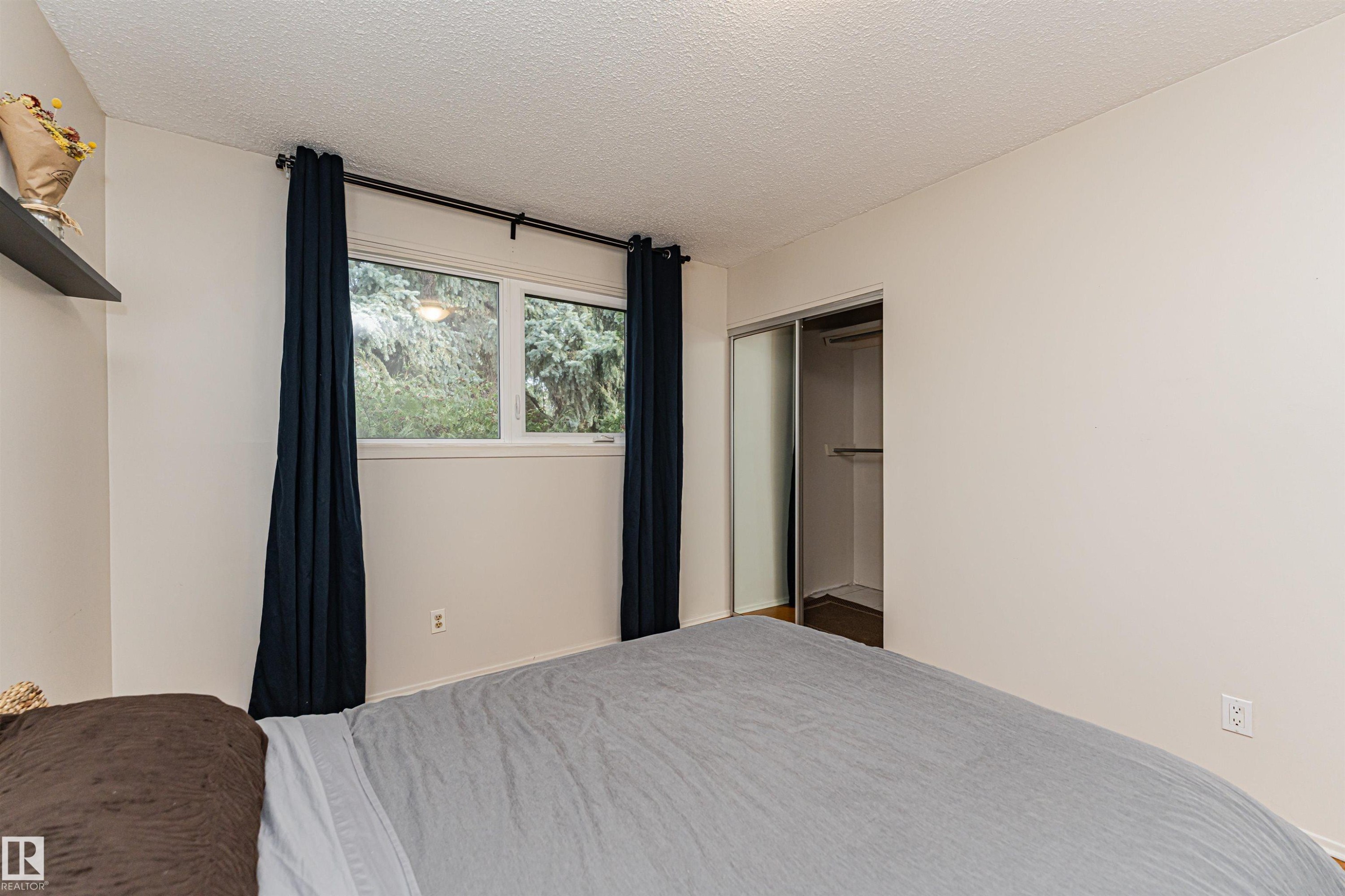 Bedroom featuring a window with exterior tree foliage, a built-in shelf, and a closet with sliding doors - 11423 50 Avenue, Edmonton, AB - Indoor Photo Showing Bedroom